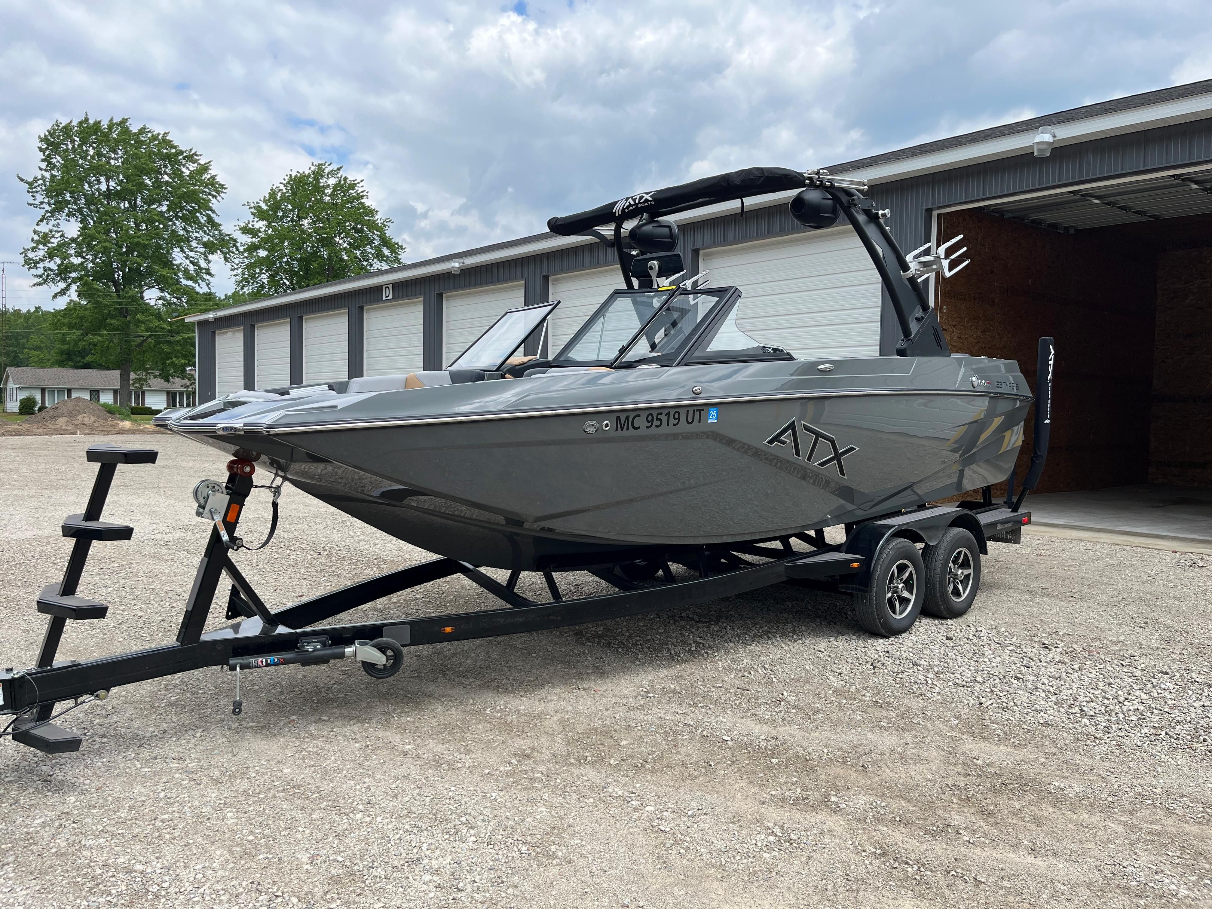 A gray 2022 ATX Surf Boat 22 Type-S on a trailer in front of a warehouse.