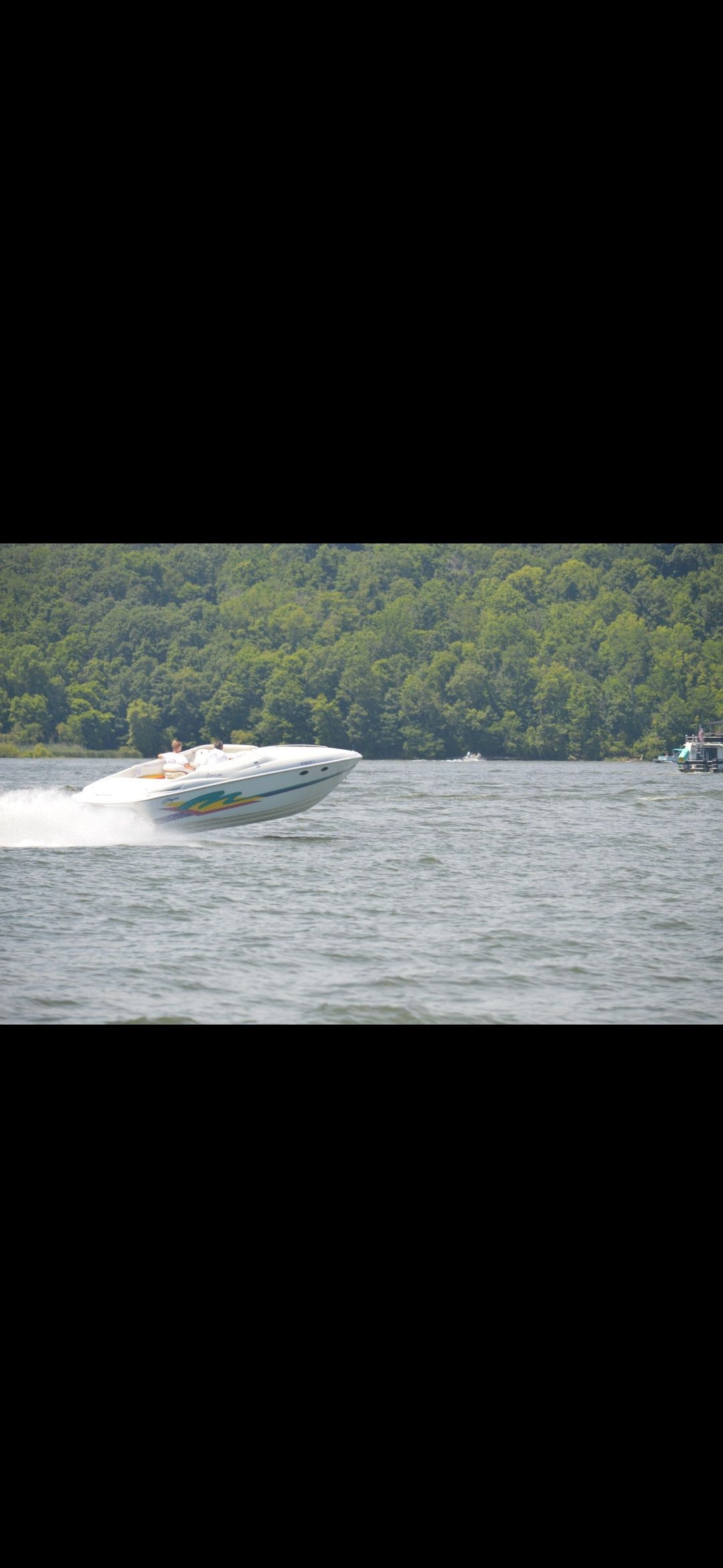 A 1996 Baja 302 Boss speeding across the water, surrounded by green hills.