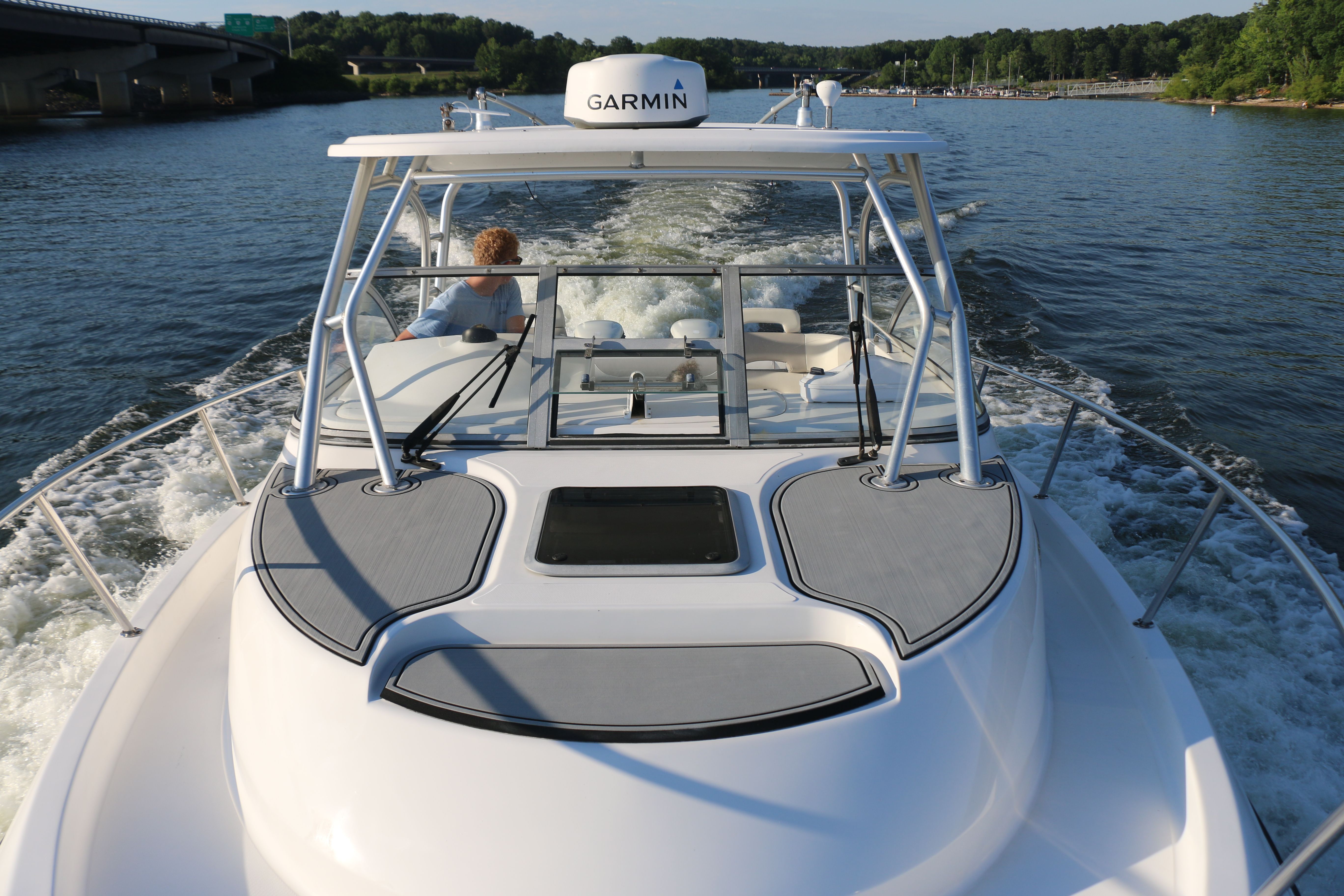 A 2006 Boston Whaler 305 Conquest cruising on a calm river with green shores.