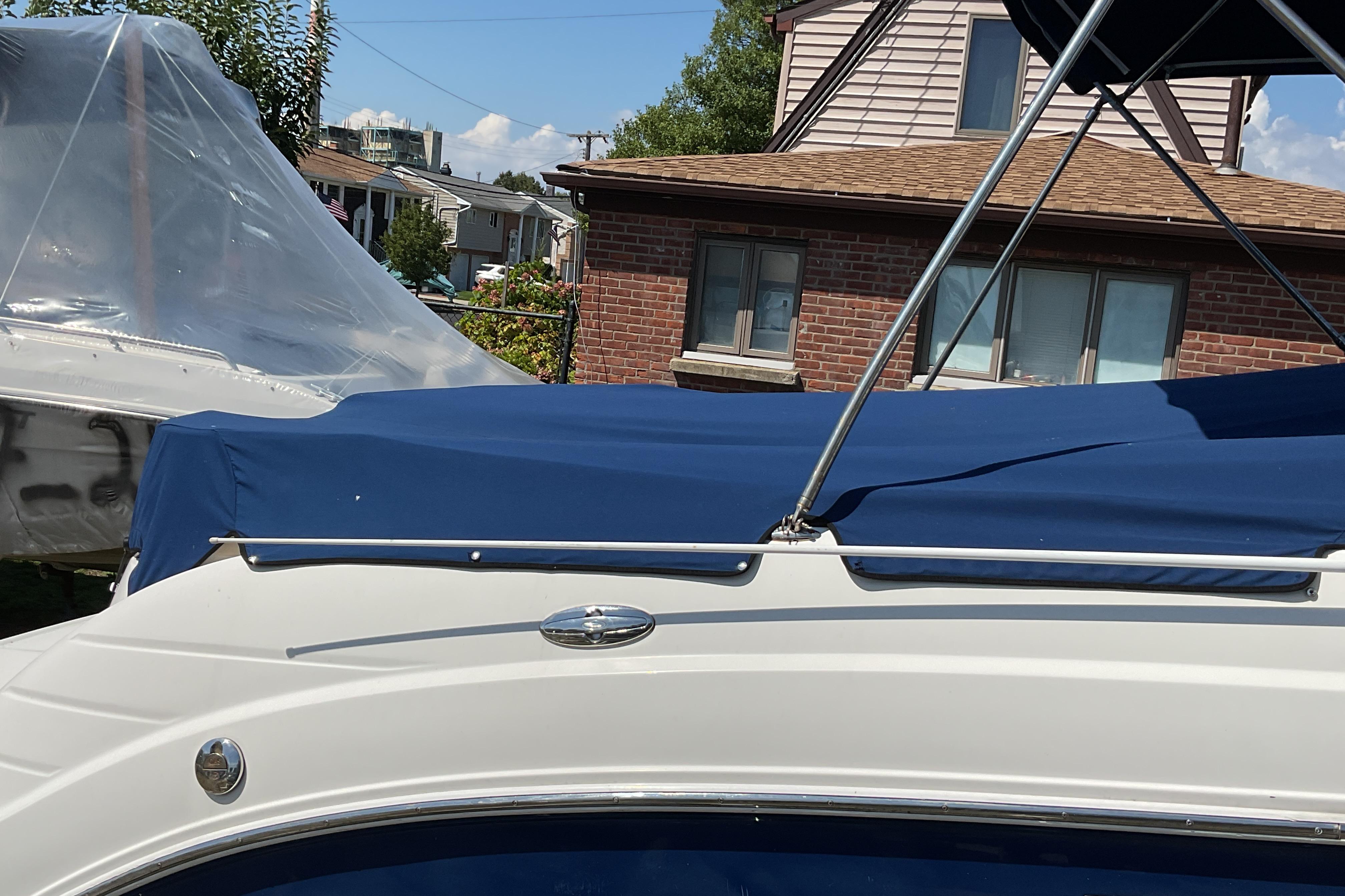 2006 Chaparral 256 SSi boat with blue cover, parked near a brick house.