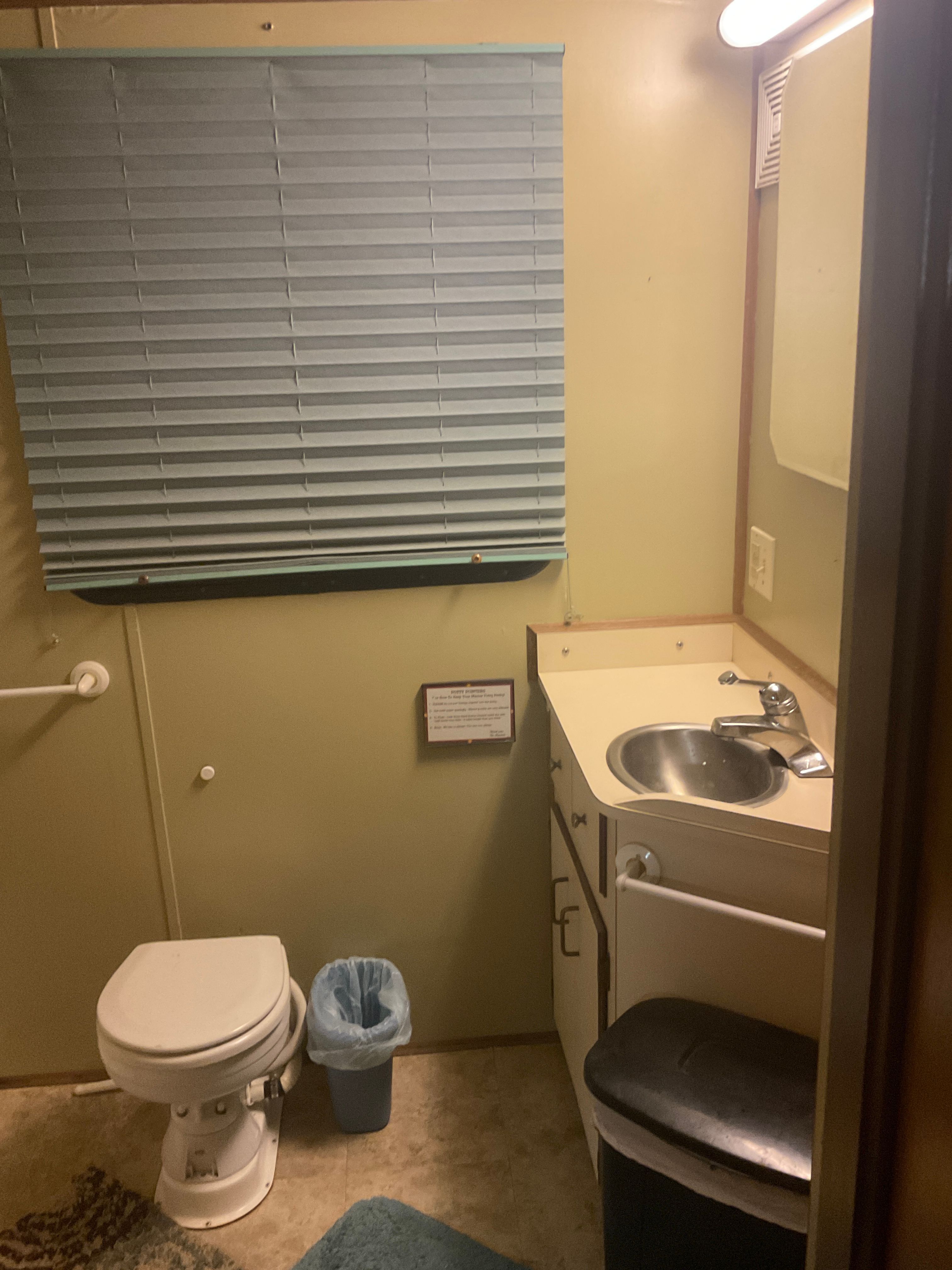 The image shows a bathroom with a toilet, sink, and window with a blind.