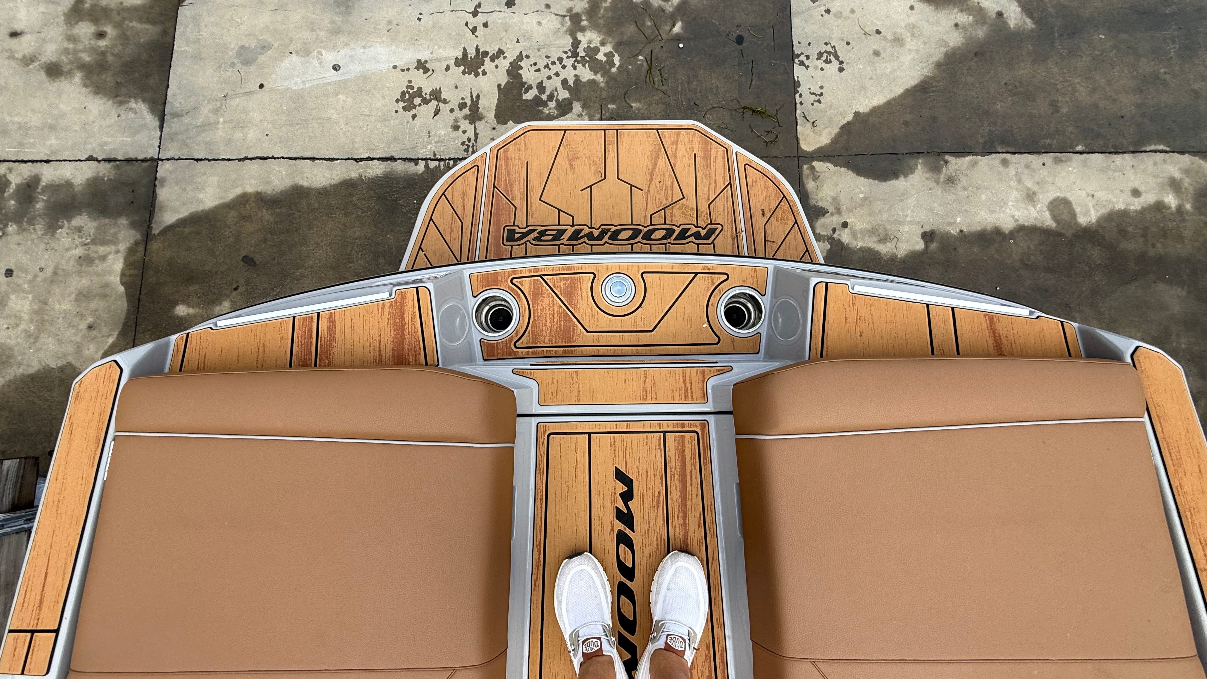 The image shows the stern of a Malibu Mojo boat with brown upholstery and wood accents.