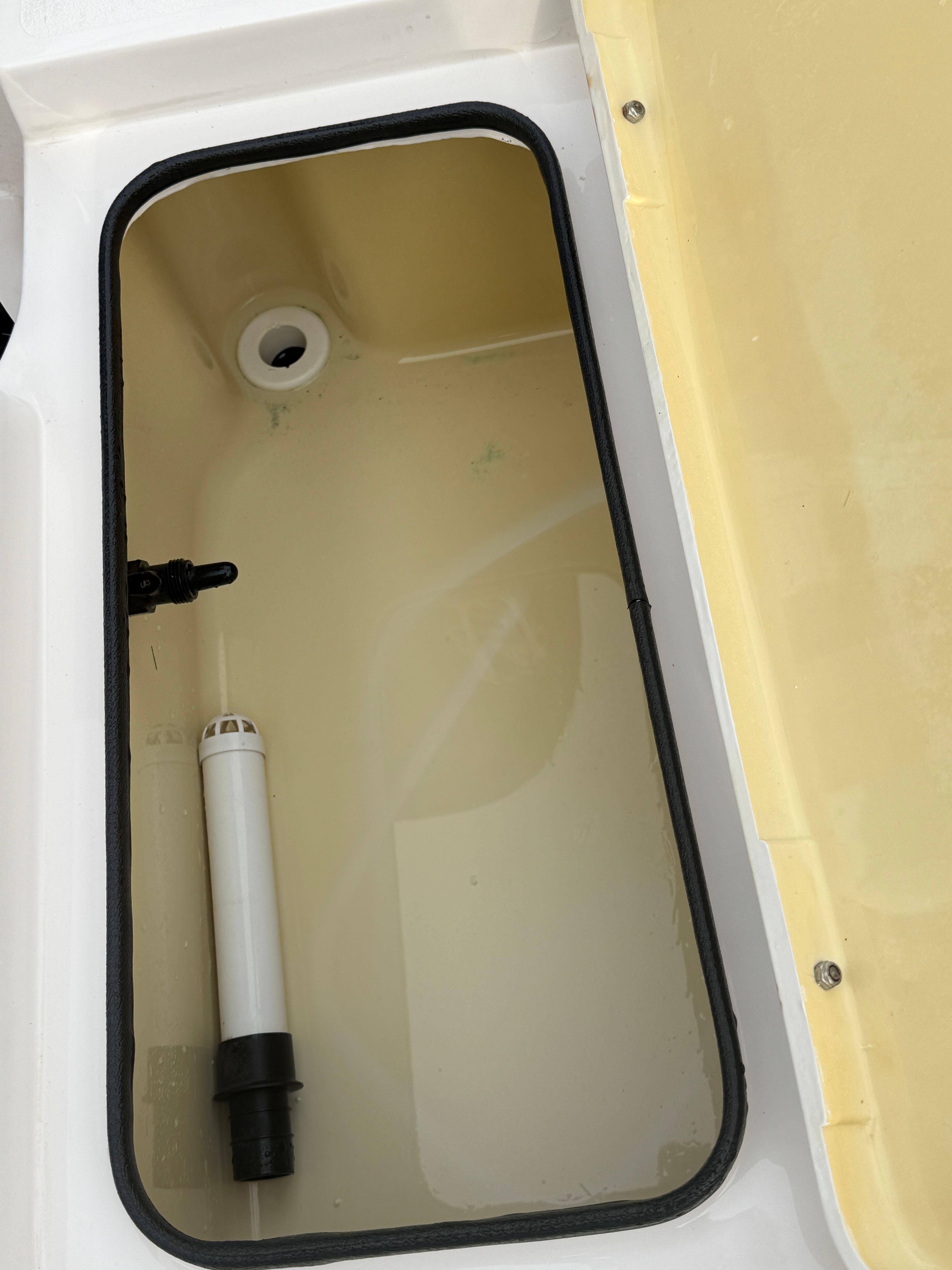 An open storage compartment with a white pipe and a drain hole.