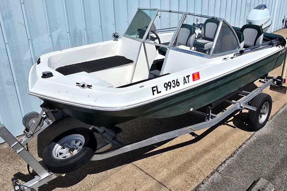 1971 Jupiter 15' Tri Hull boat on trailer, white and green, parked by a building.
