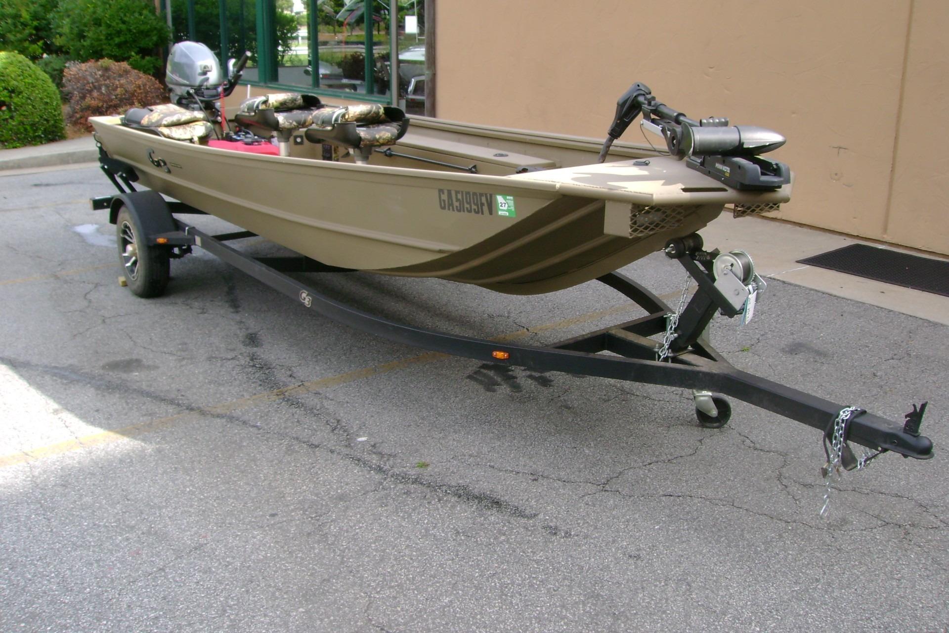 2023 G3 1652 DK boat on trailer, parked outdoors, featuring camouflage seating and motor.