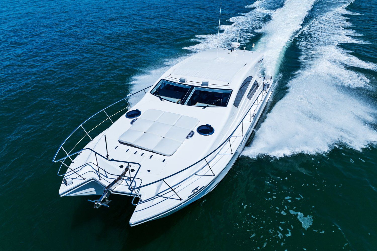 A white catamaran speeds across blue water, leaving a trail of spray behind.