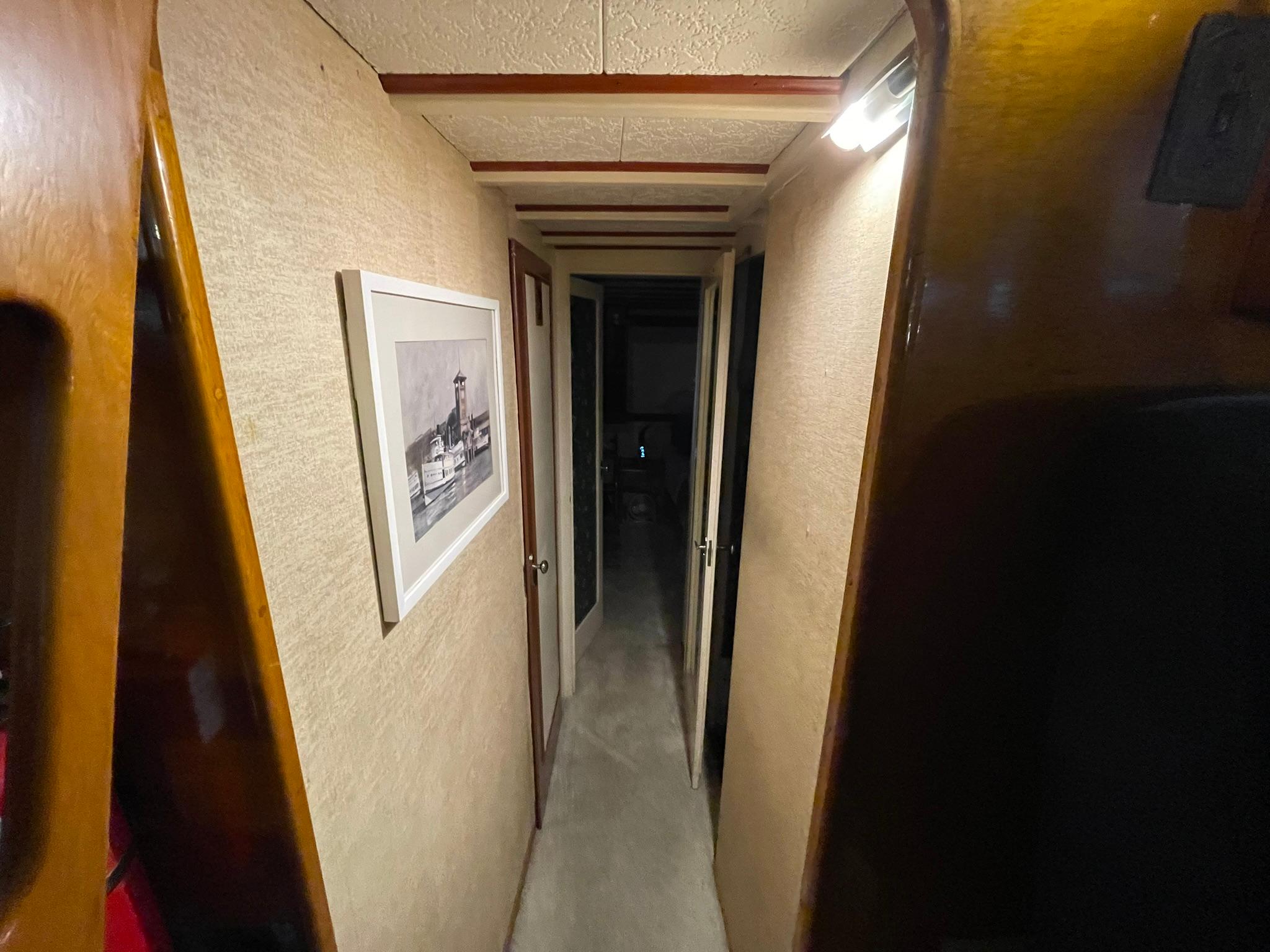 Narrow hallway inside a 1951 Chris-Craft Catalina boat, featuring wood paneling and framed artwork.