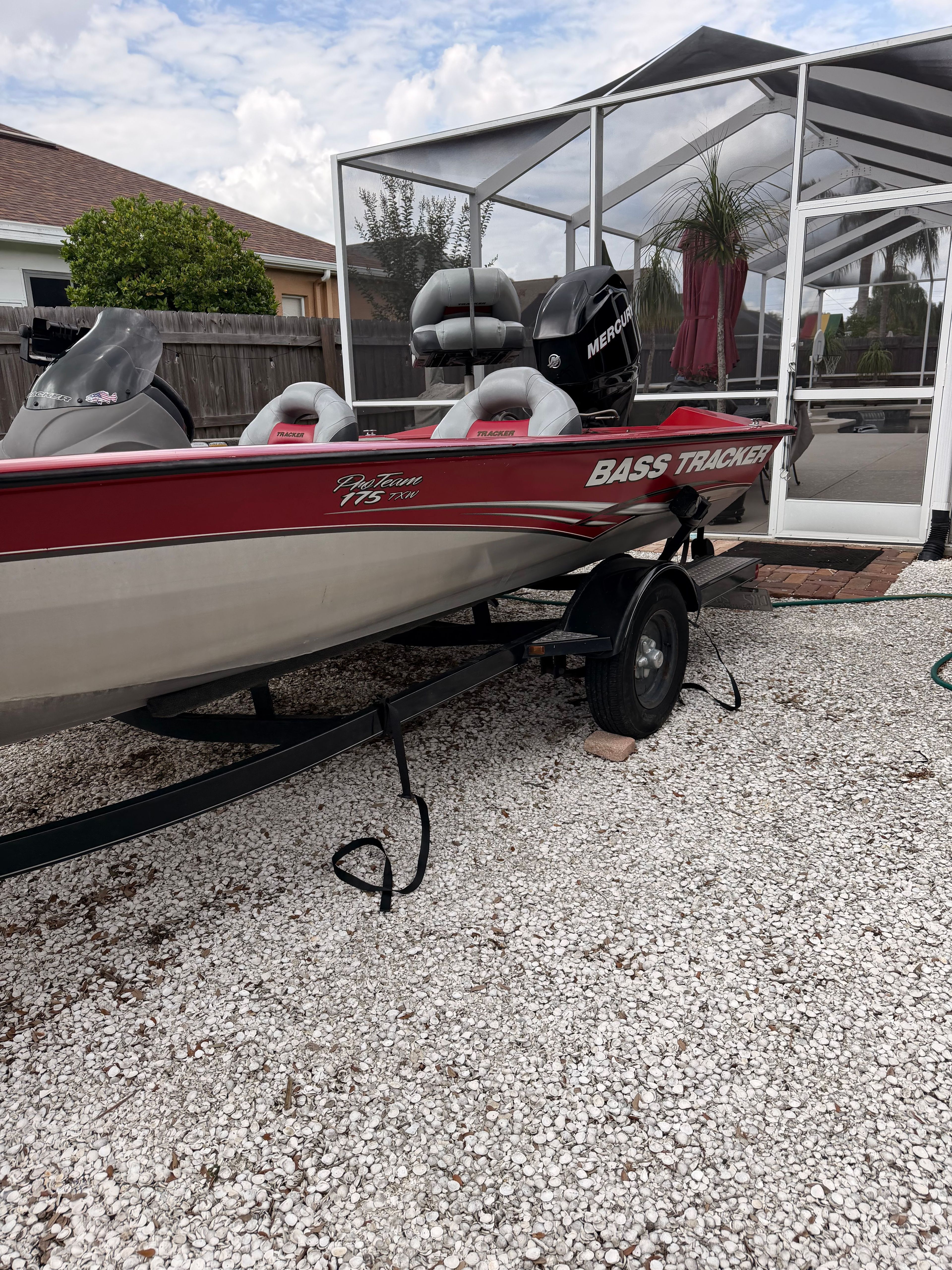A red 2011 Bass Tracker PRO TEAM 175 TXW boat on a trailer on gravel.