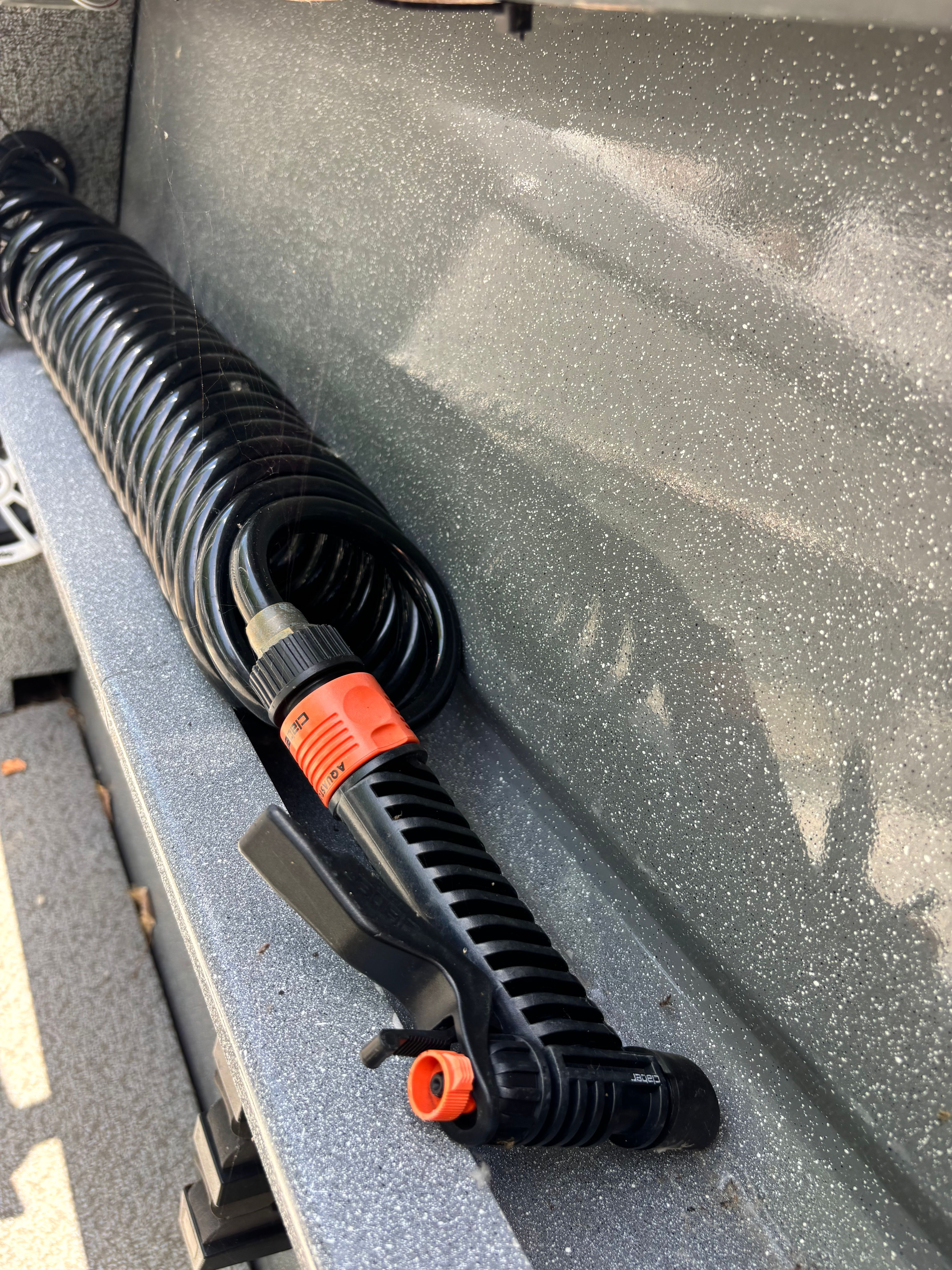 A black coiled hose with an orange nozzle rests on a gray surface.