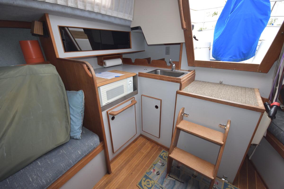 Interior of a sailboat with sink, microwave, and wooden details.