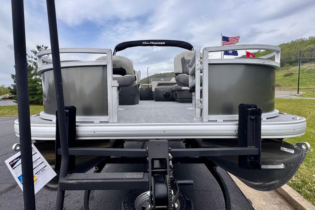 2026 Sun Tracker Bass Buggy 18 DLX pontoon boat on trailer, flags in background.
