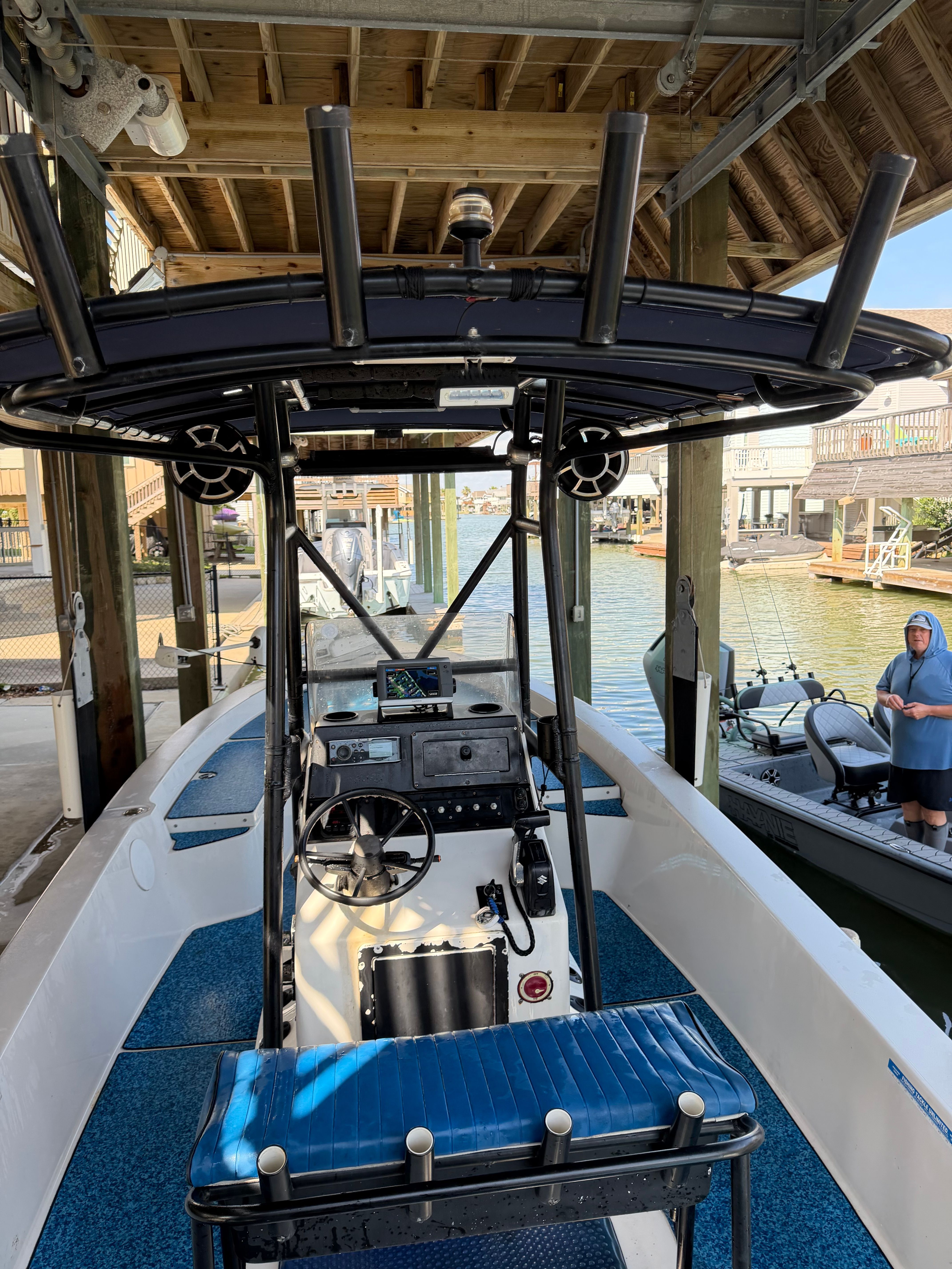 A white boat with blue flooring is docked under a covered area.