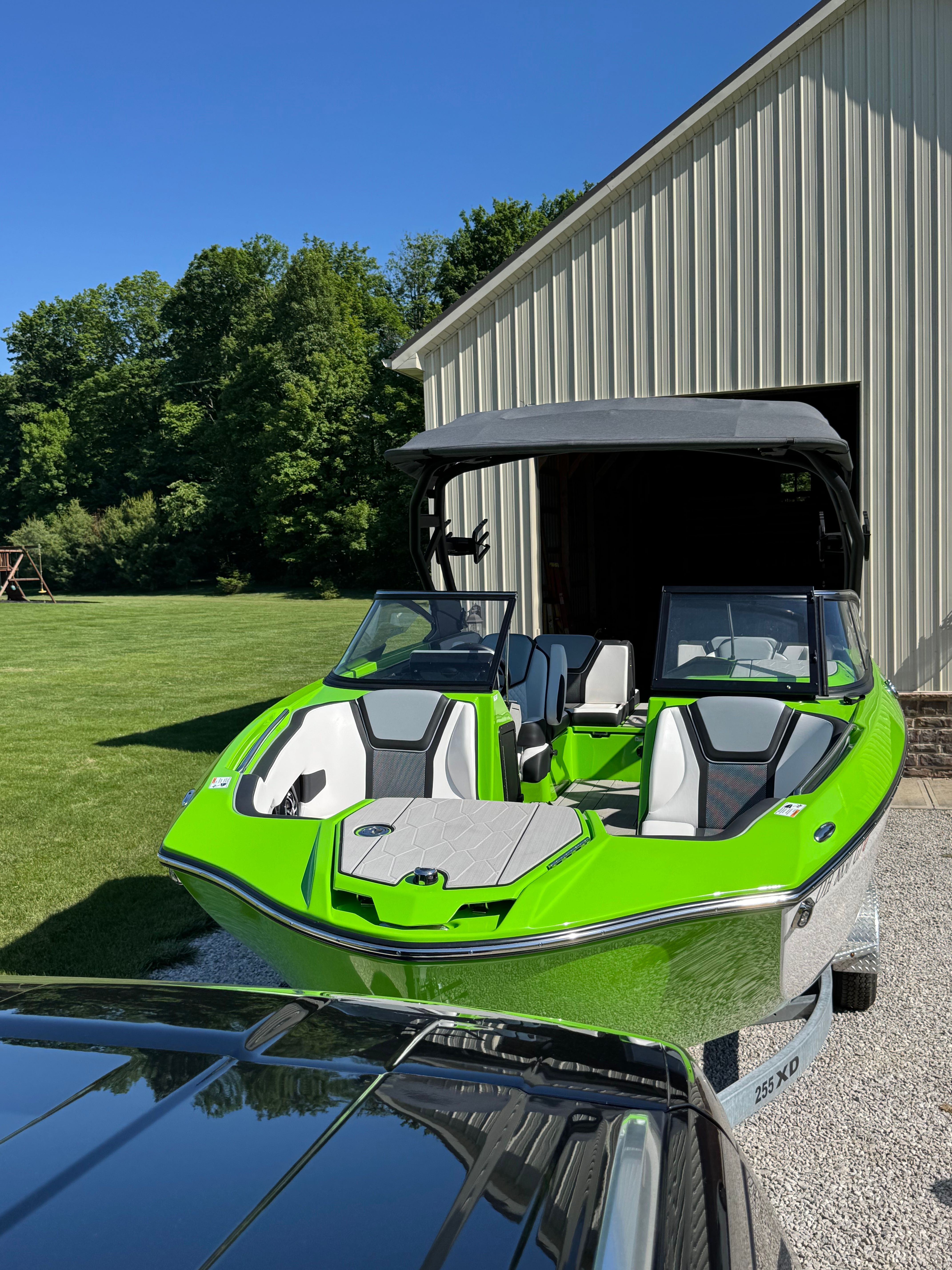 A green 2022 Yamaha 255XD boat on a trailer beside a building.