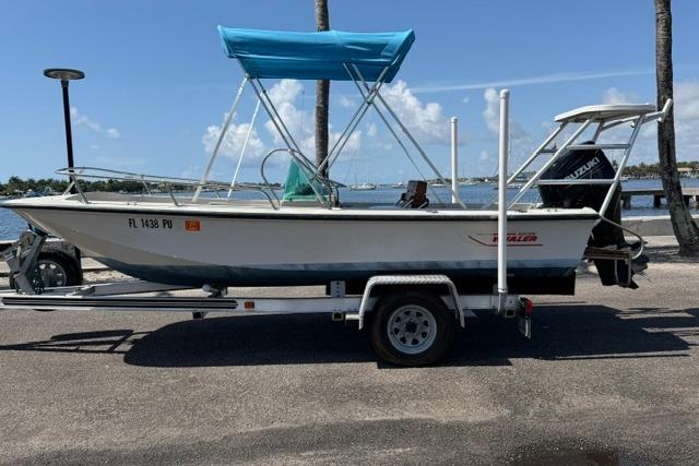 1990 Boston Whaler 17 Newport boat on trailer with blue canopy, parked near waterfront.
