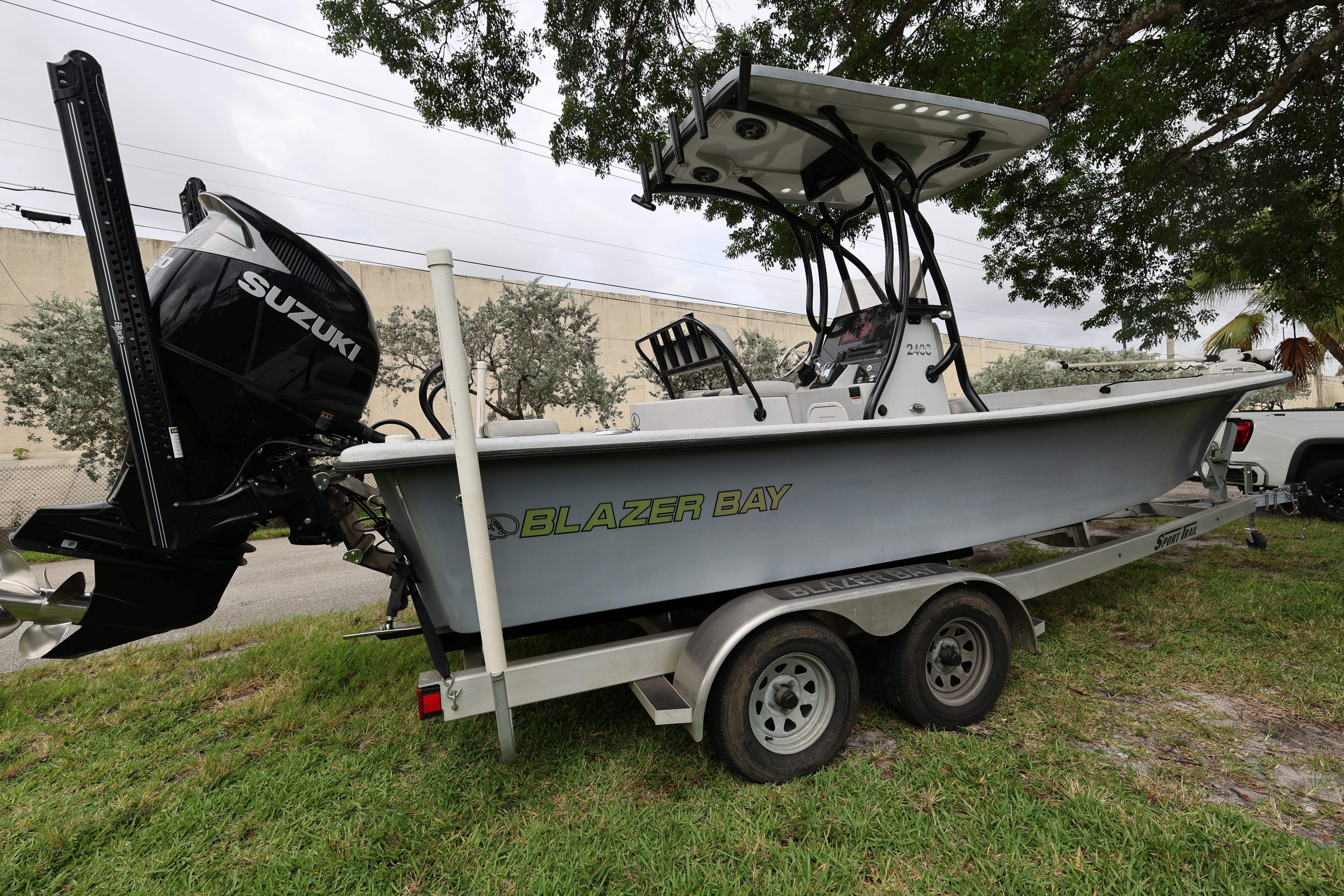 2021 Blazer Bay 2400 boat with Suzuki engine on a trailer, parked on grass.