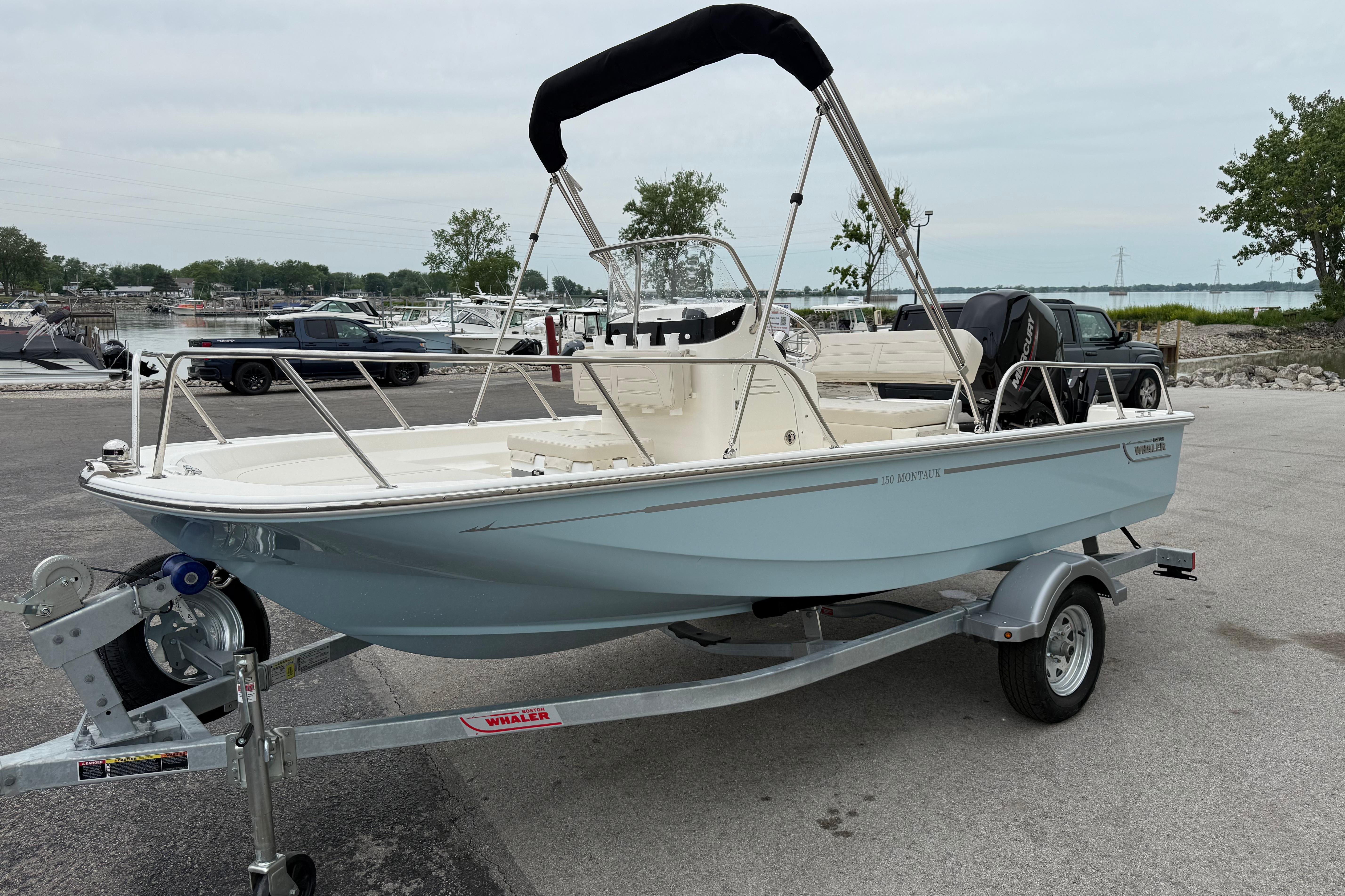 2026 Boston Whaler 150 Montauk boat on trailer, parked near marina with scenic background.