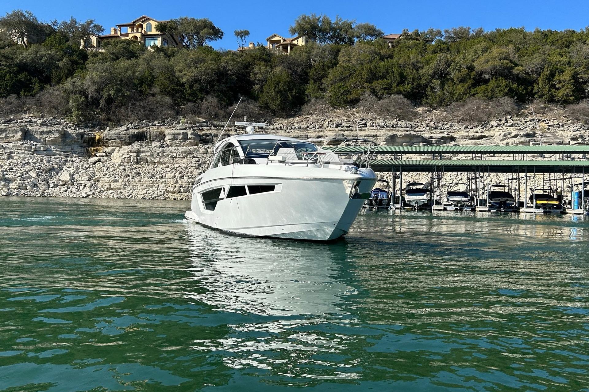 2021 Cruisers Yachts 50 Cantius on serene lake with rocky shoreline backdrop.