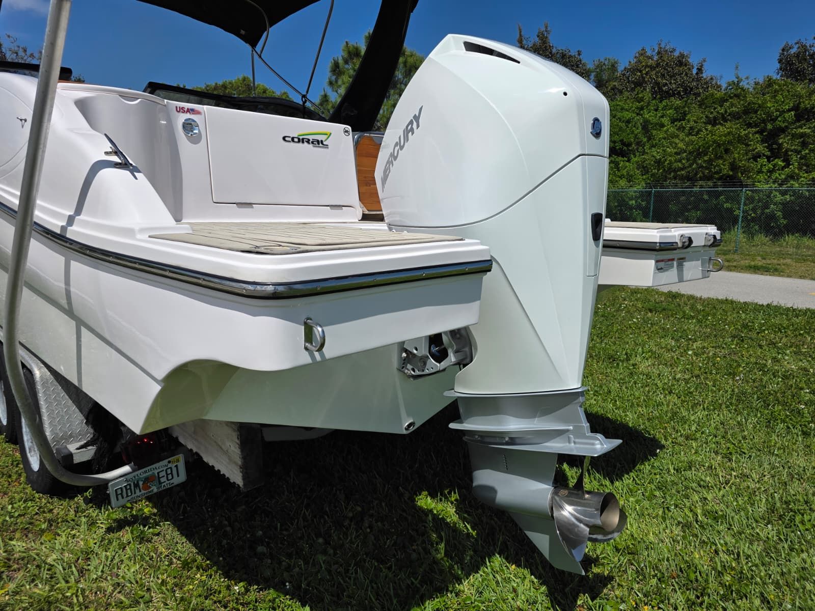 The image shows a white boat with a Mercury outboard motor on a green lawn.