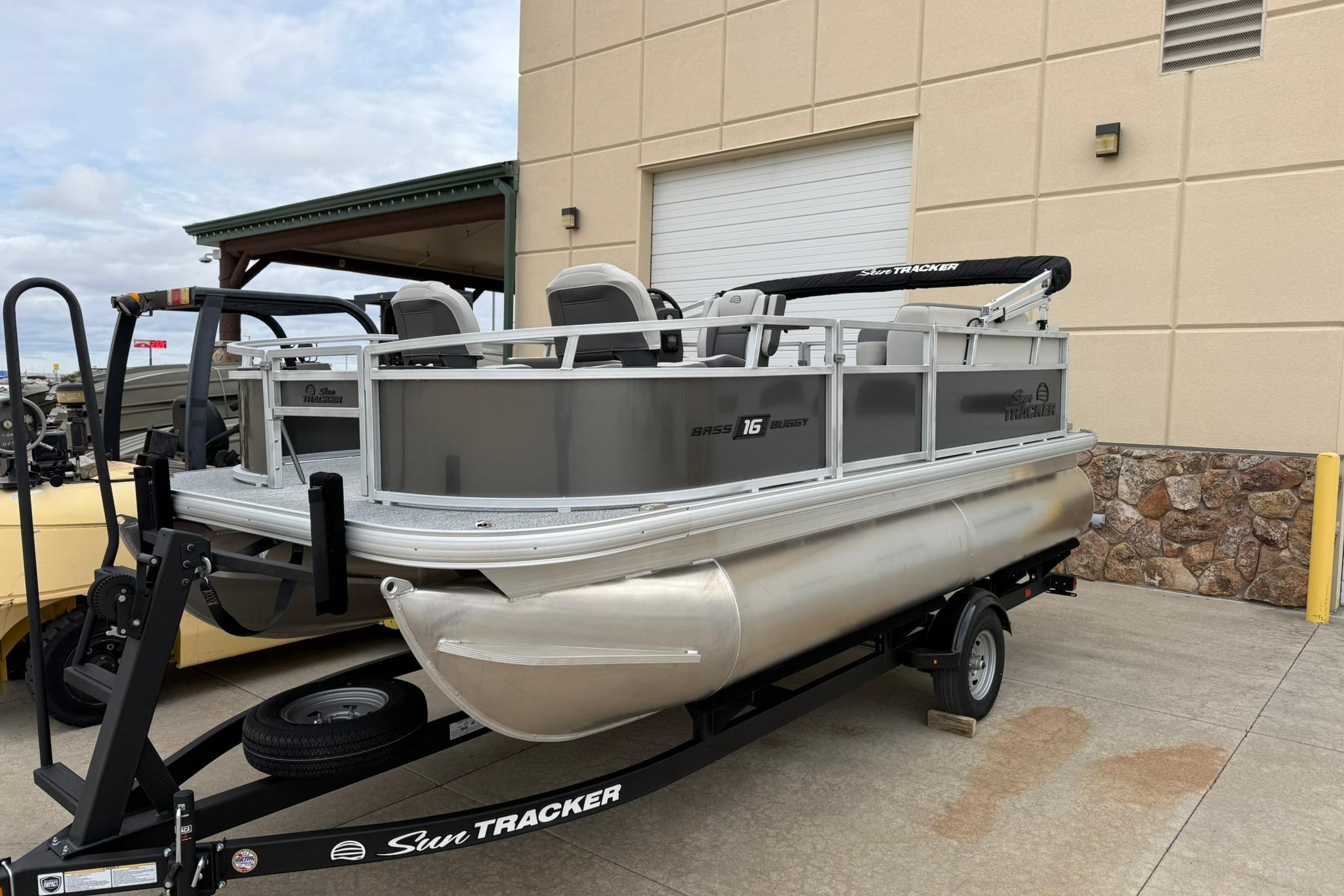 2026 Sun Tracker Bass Buggy 16 XL Select pontoon boat on trailer, parked outdoors.