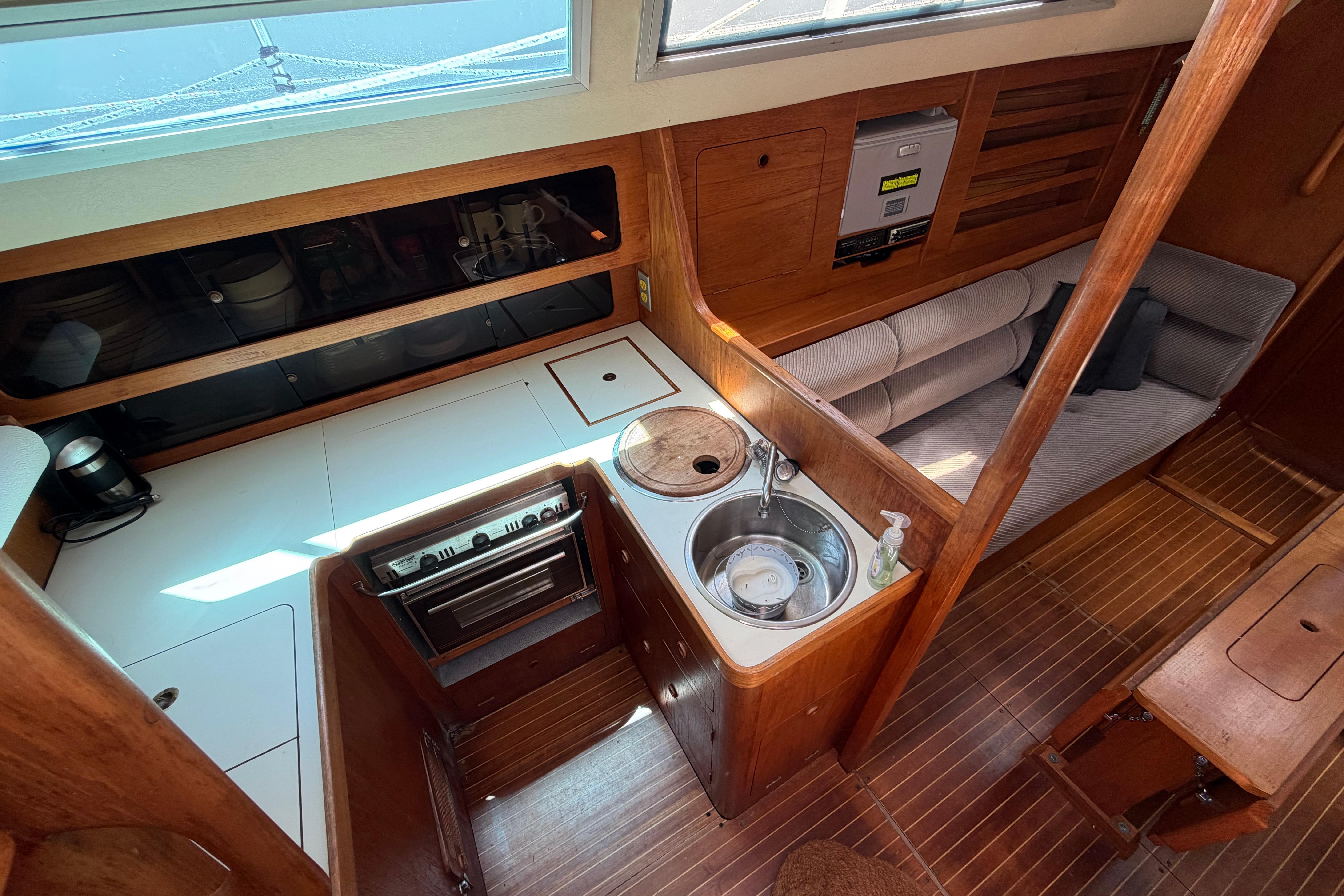 1987 Moody 376 yacht interior with wooden cabinetry, compact kitchen, and cozy seating area.