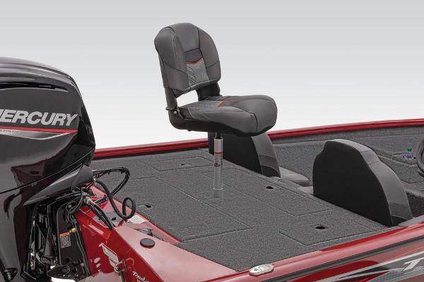 A red boat with a Mercury engine and an elevated seat on gray carpeted flooring.