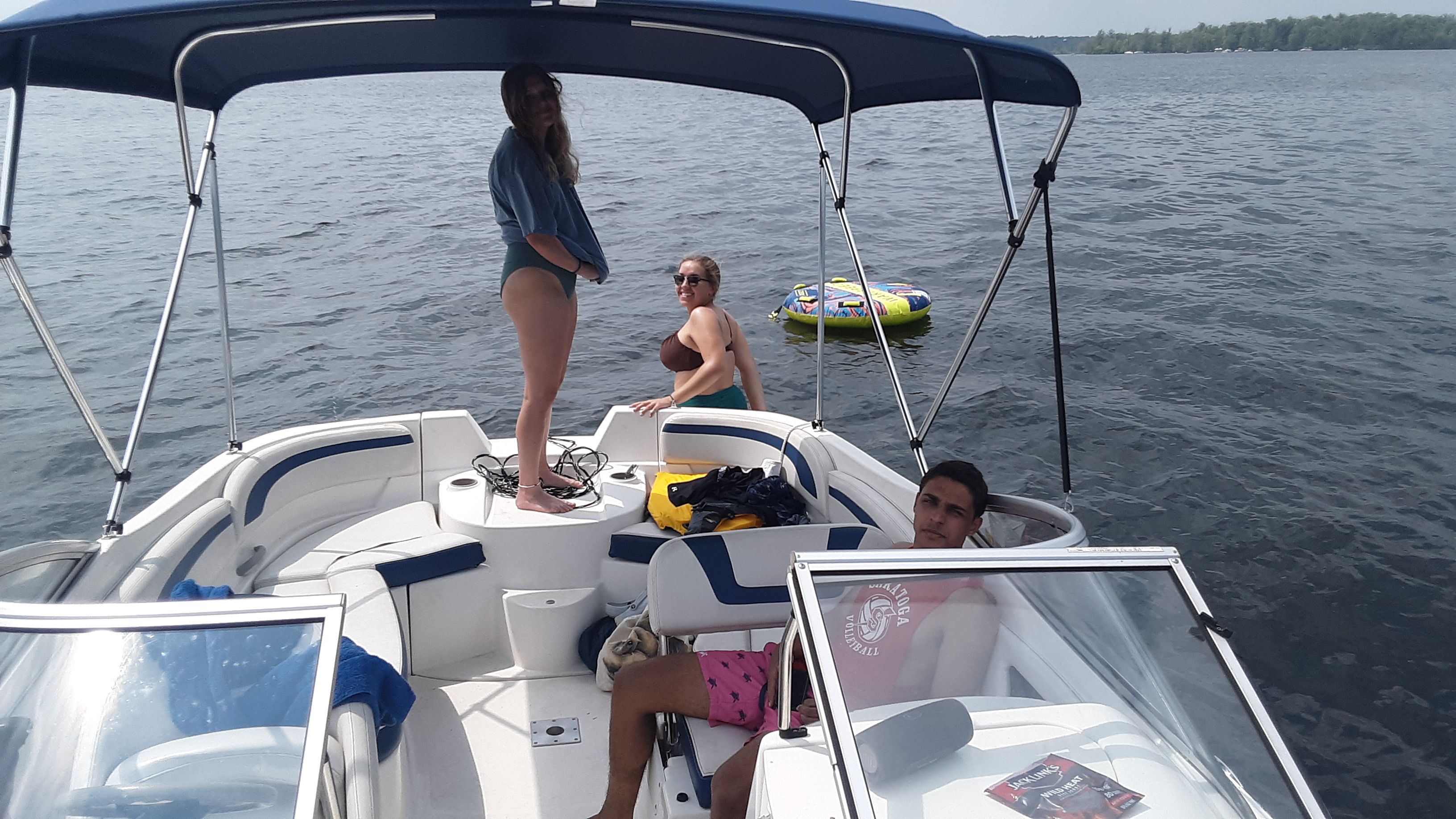 Three people relax on a Bayliner 210 Classic boat on a calm lake.