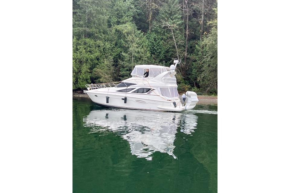 2006 Silverton 38 Sport Bridge yacht on calm water, surrounded by lush greenery.