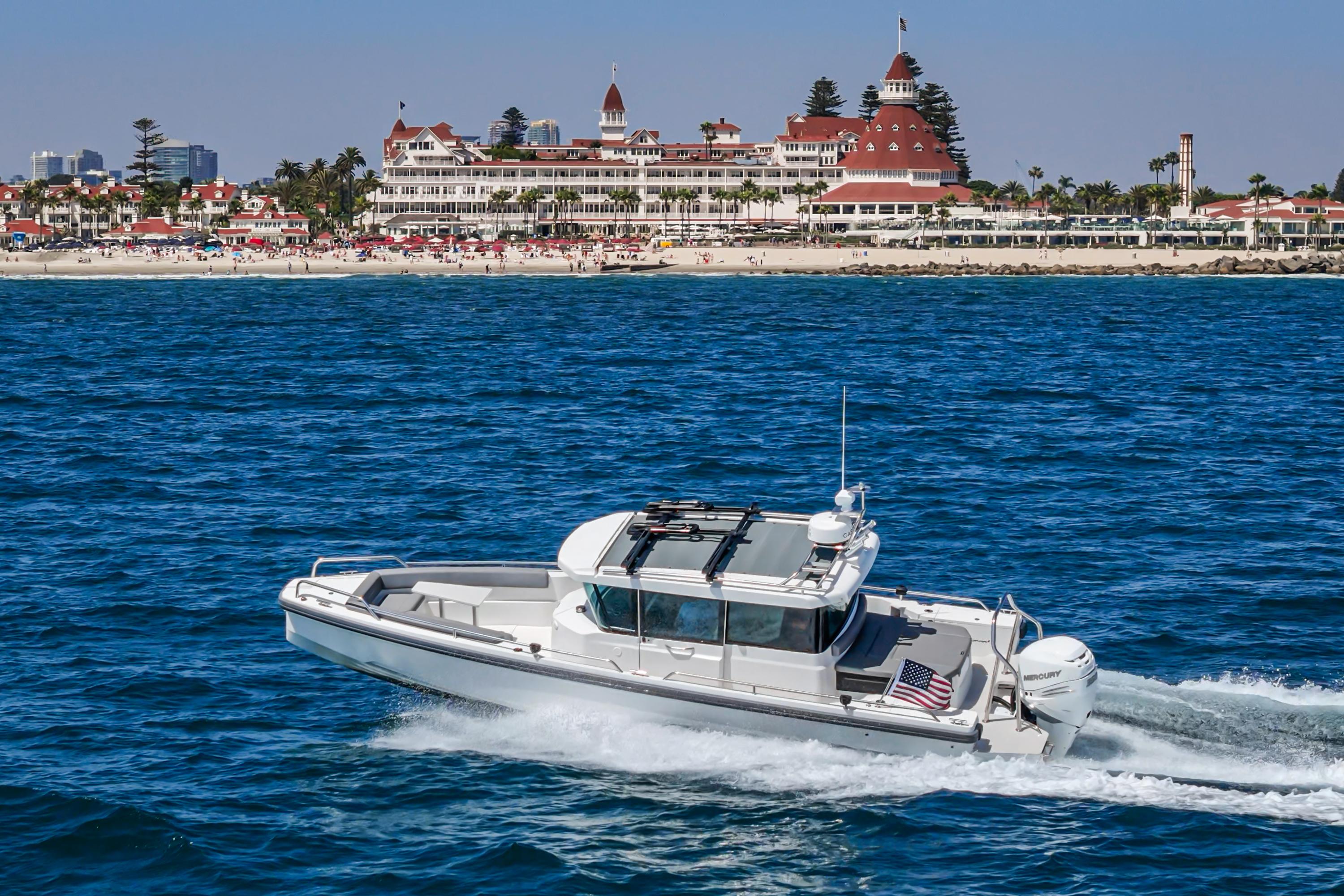2019 Axopar 28 CABIN boat cruising near a historic beachfront hotel.