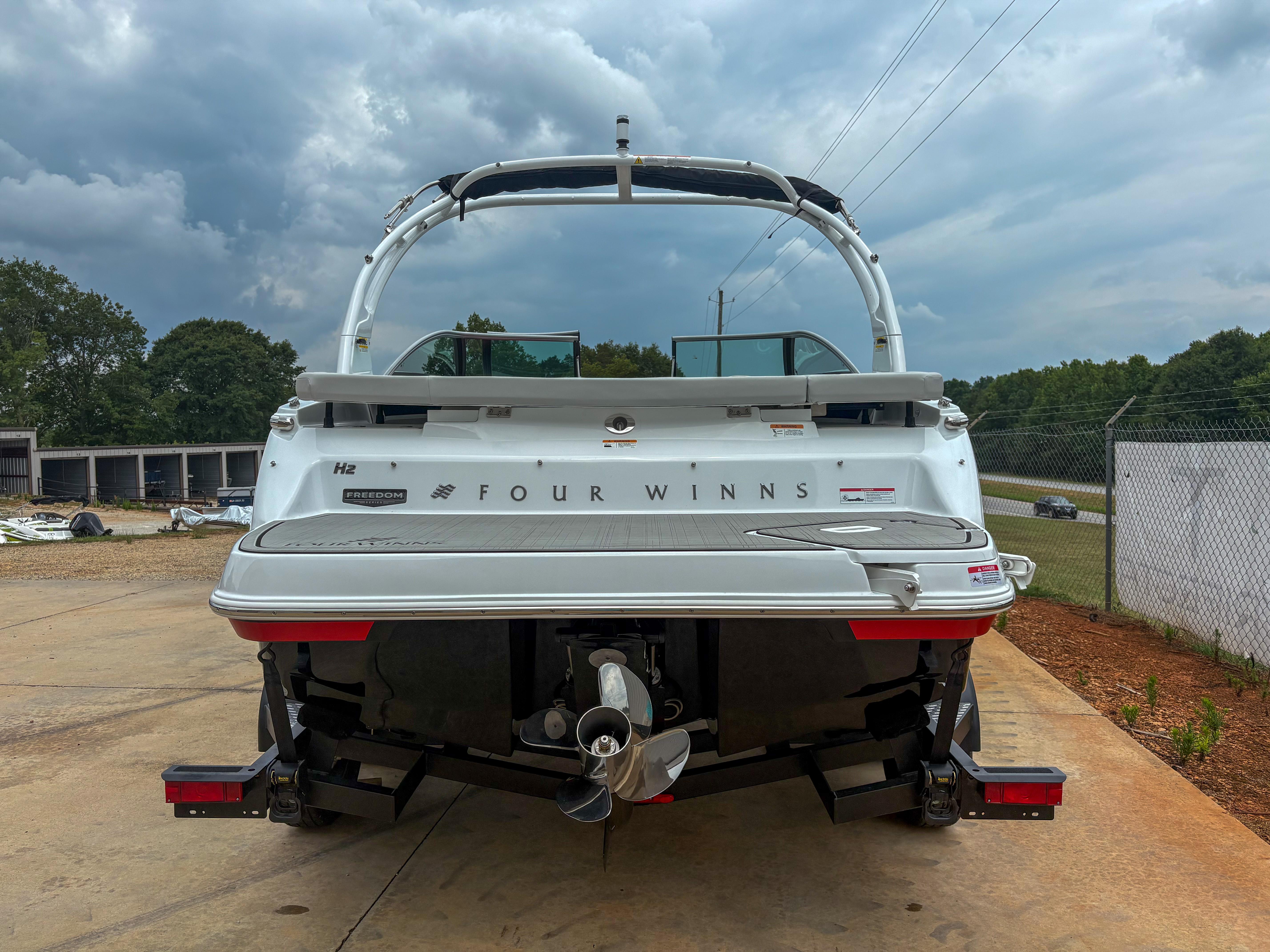 2026 Four Winns H2 Freedom boat, rear view, parked on concrete under cloudy sky.