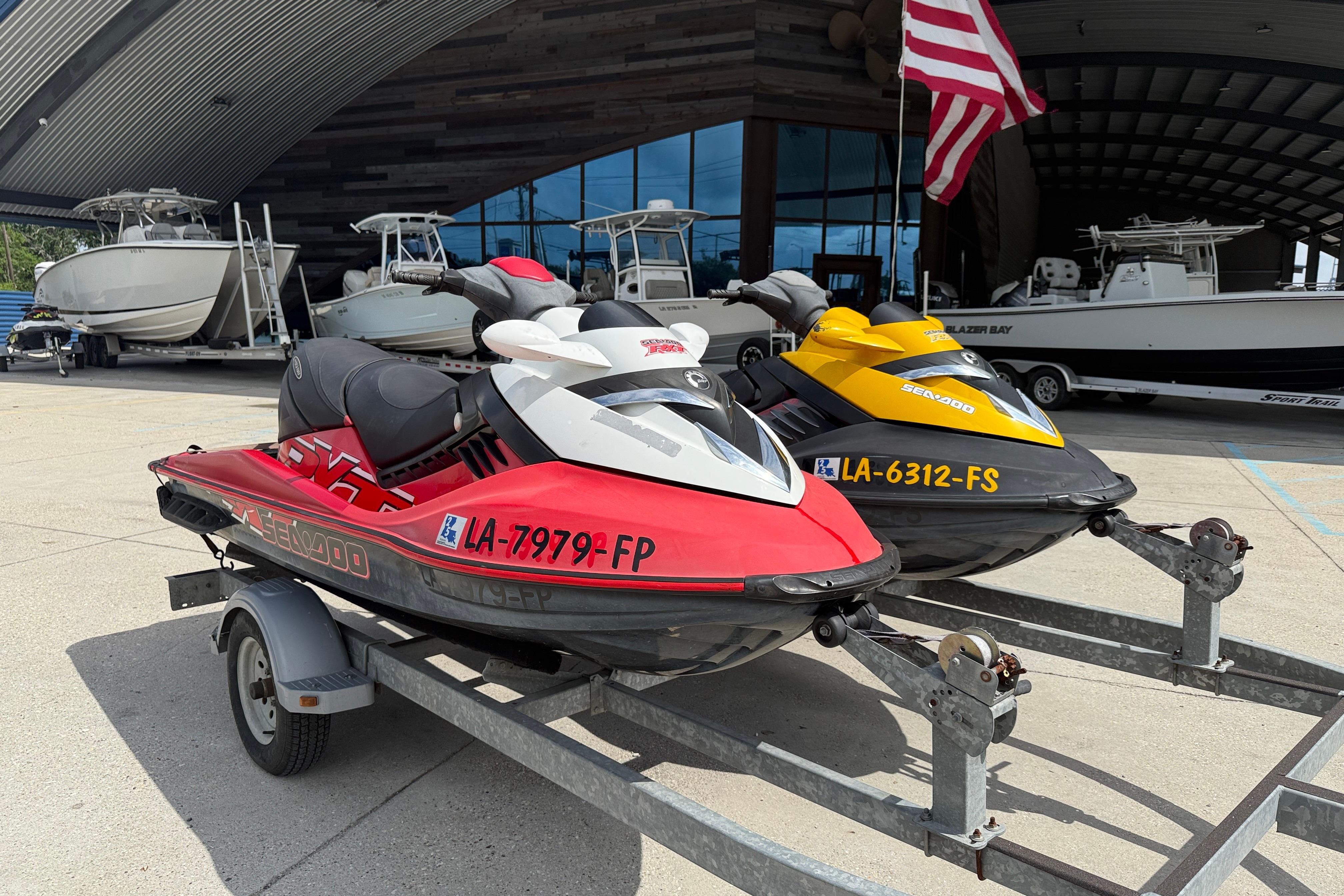 Two 2007 Sea-Doo RXT 215 jet skis on a trailer, parked near boats.