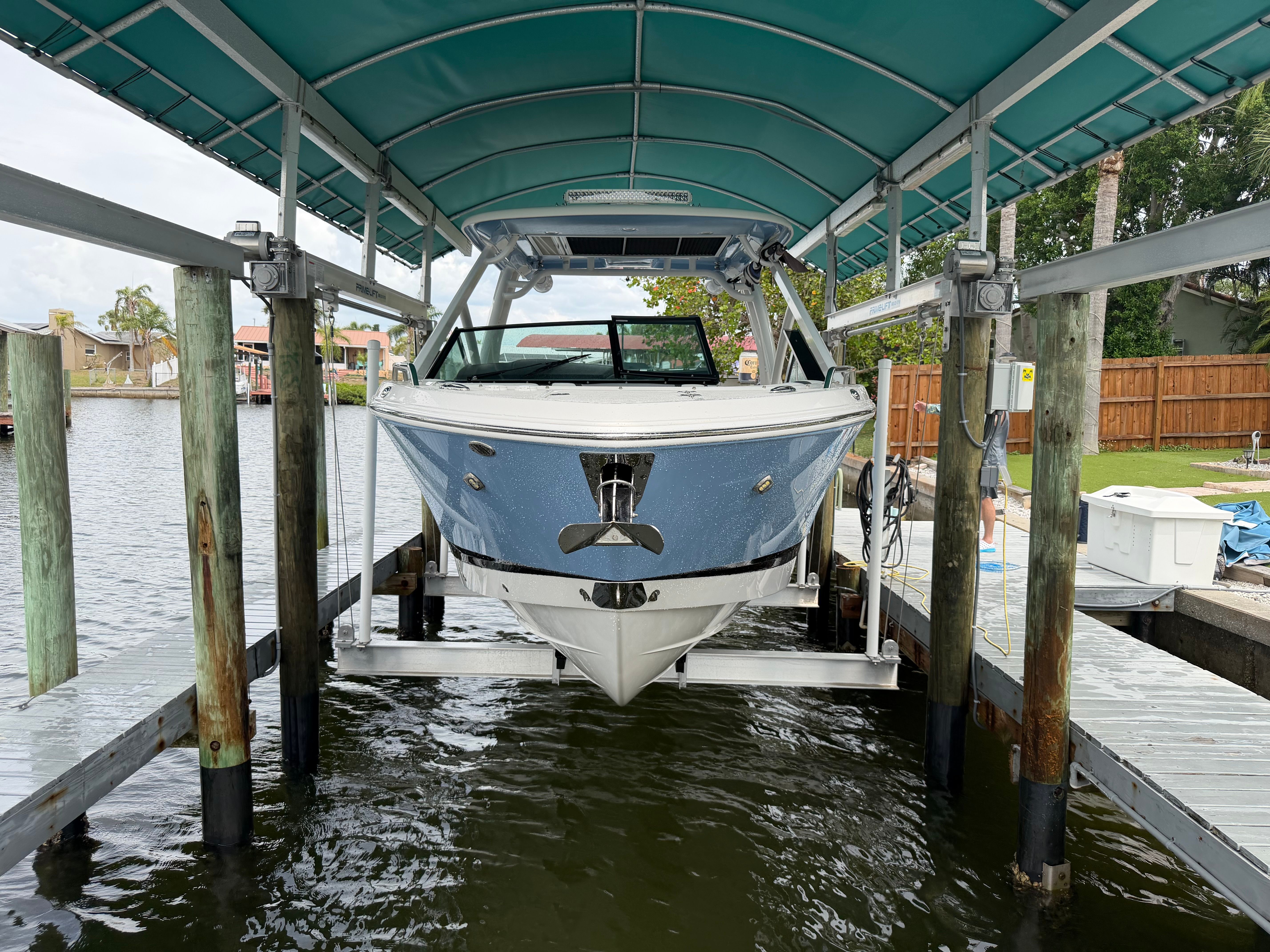 A Chaparral 280 OSX boat is parked on a covered boat lift above the water.