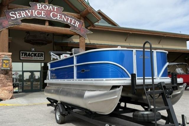 2026 Sun Tracker Party Barge 16 DLX at boat service center, blue exterior, on trailer.