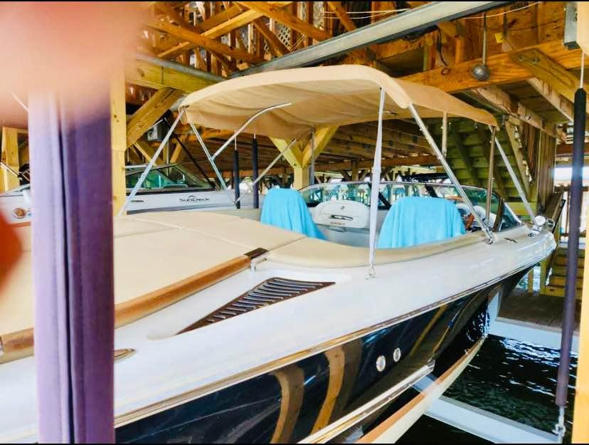 2016 Chris-Craft Carina 21 boat docked under wooden shelter with beige canopy.