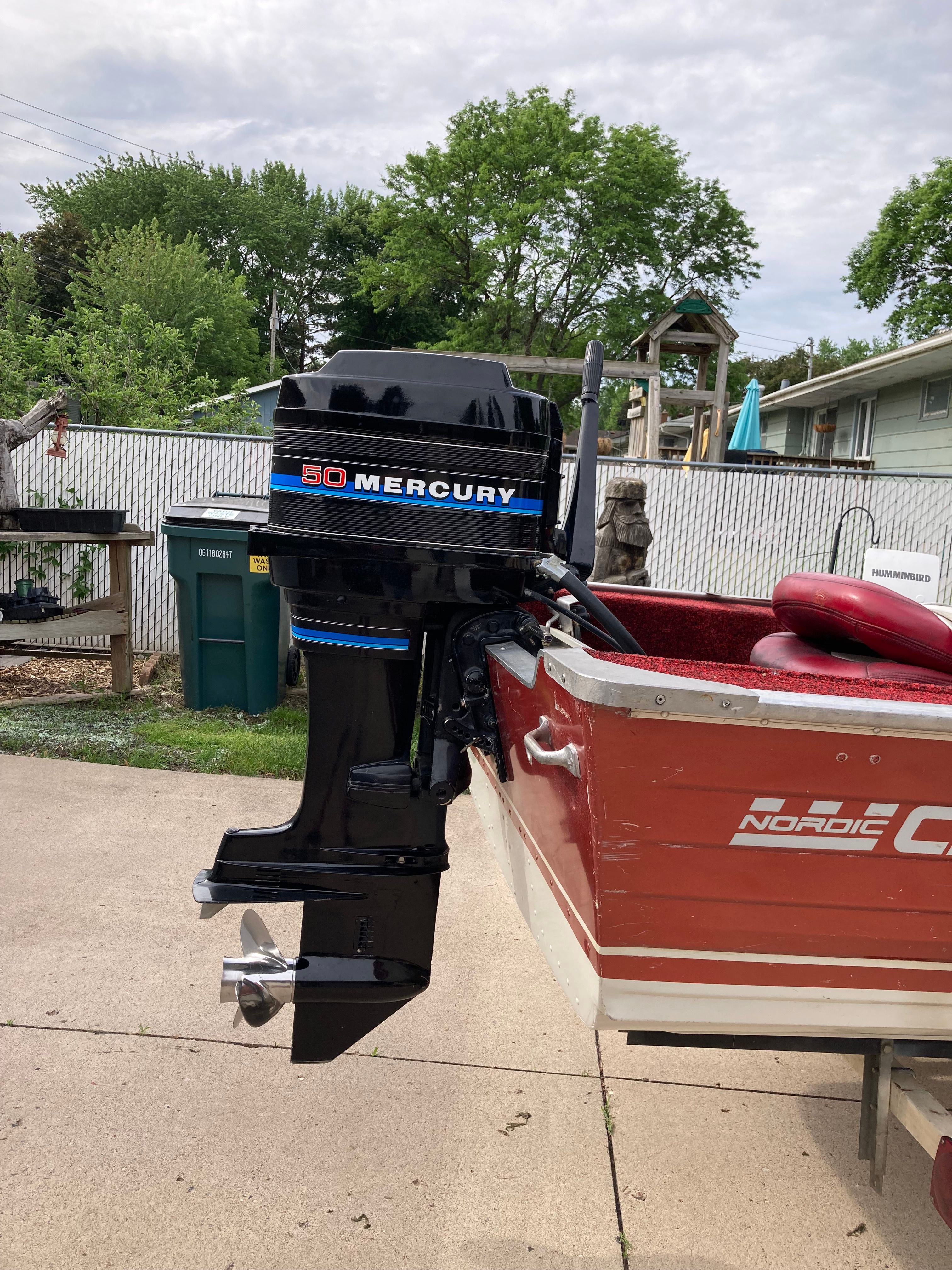 A red boat with a black Mercury outboard motor is parked on a driveway.