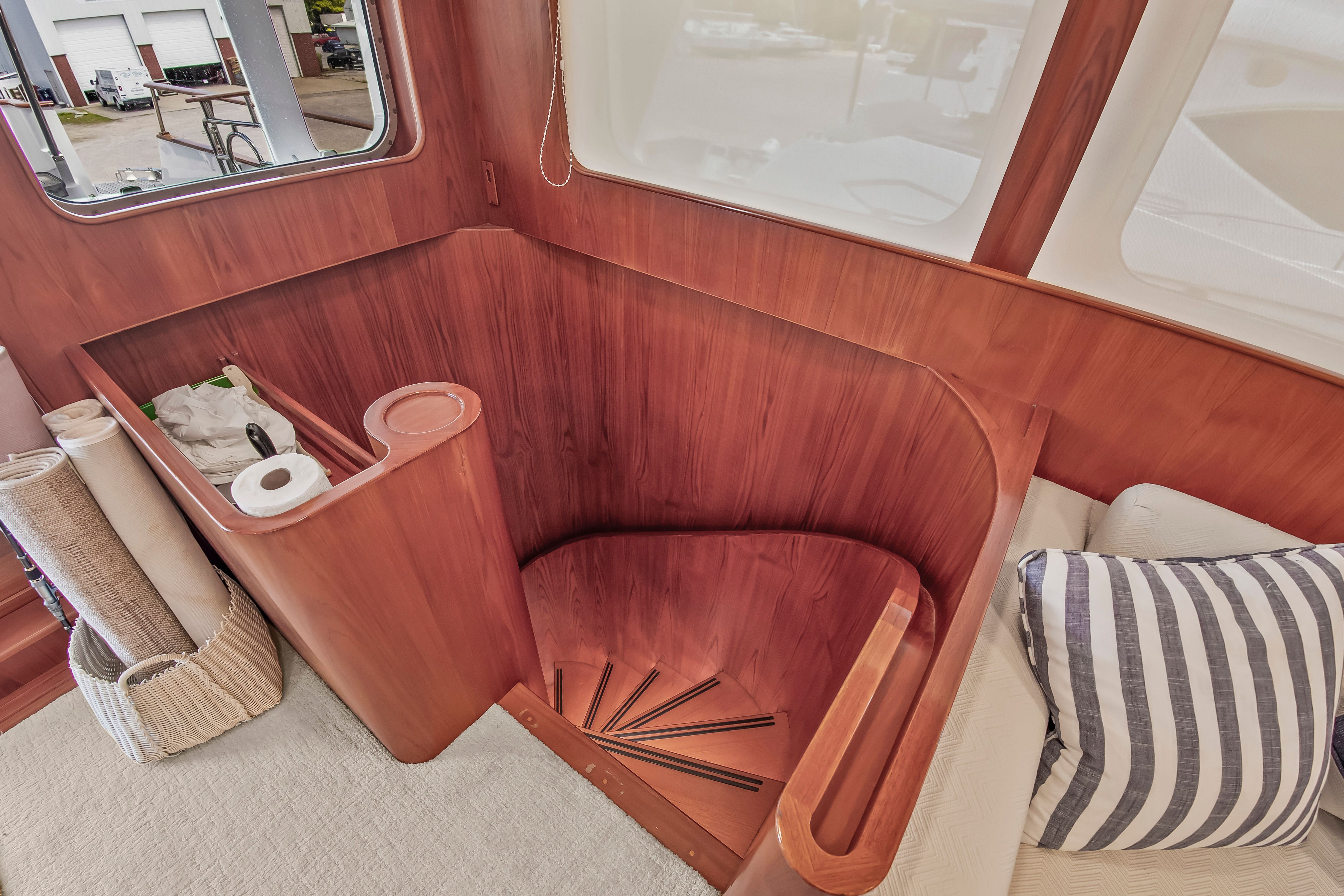 Wooden staircase in a yacht with elegant curve and window in the background.
