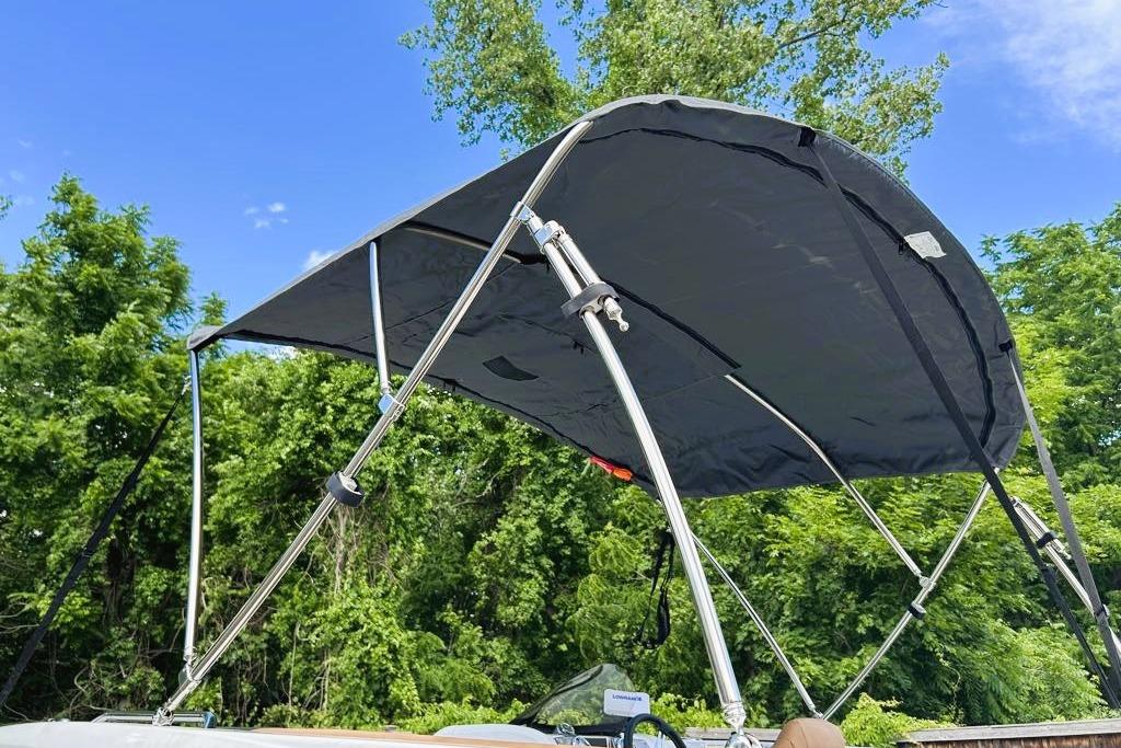 2026 Tahoe 2150 boat with a black canopy against a lush green backdrop.
