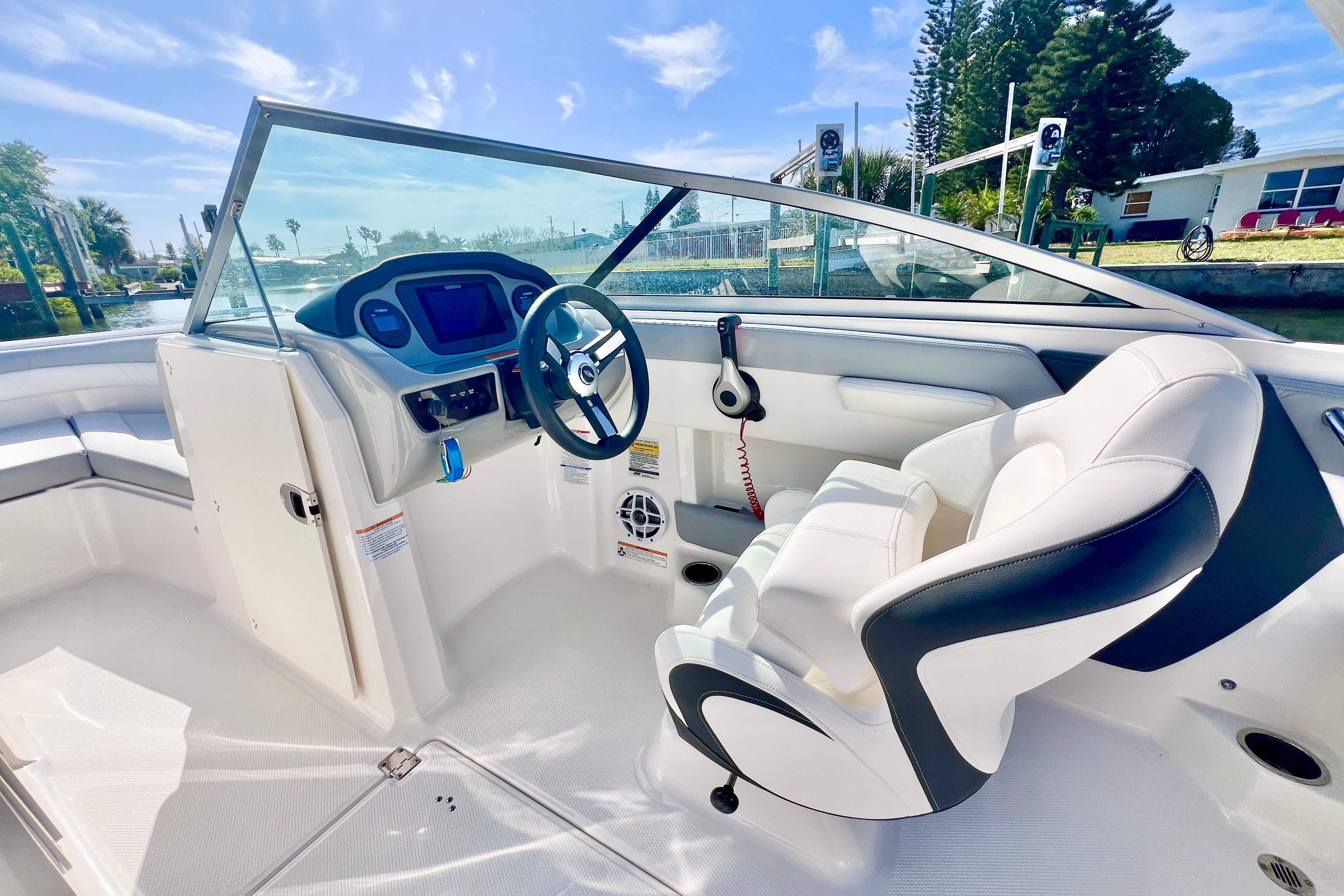 2023 Chaparral 21 SSi OB boat interior with steering wheel and seating, docked by a scenic waterfront.