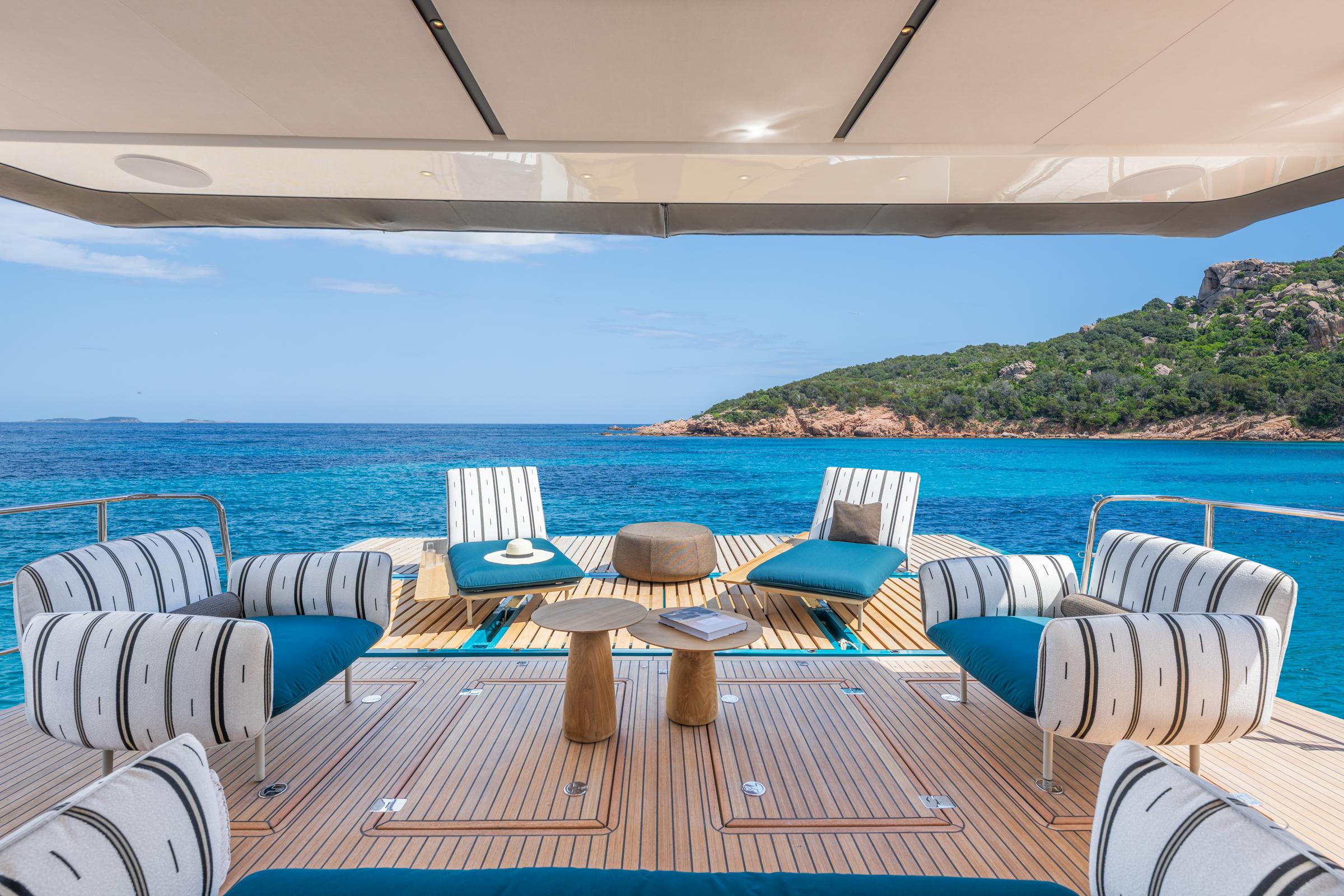 Luxurious Lagoon Eighty 2 yacht deck with stylish seating, overlooking serene blue waters and lush island.