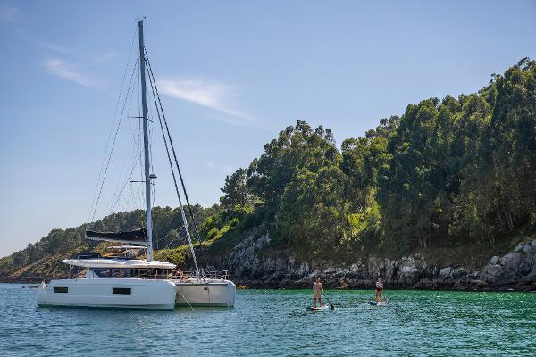 2025 Lagoon 43 yacht near paddleboarders, scenic coastal backdrop.