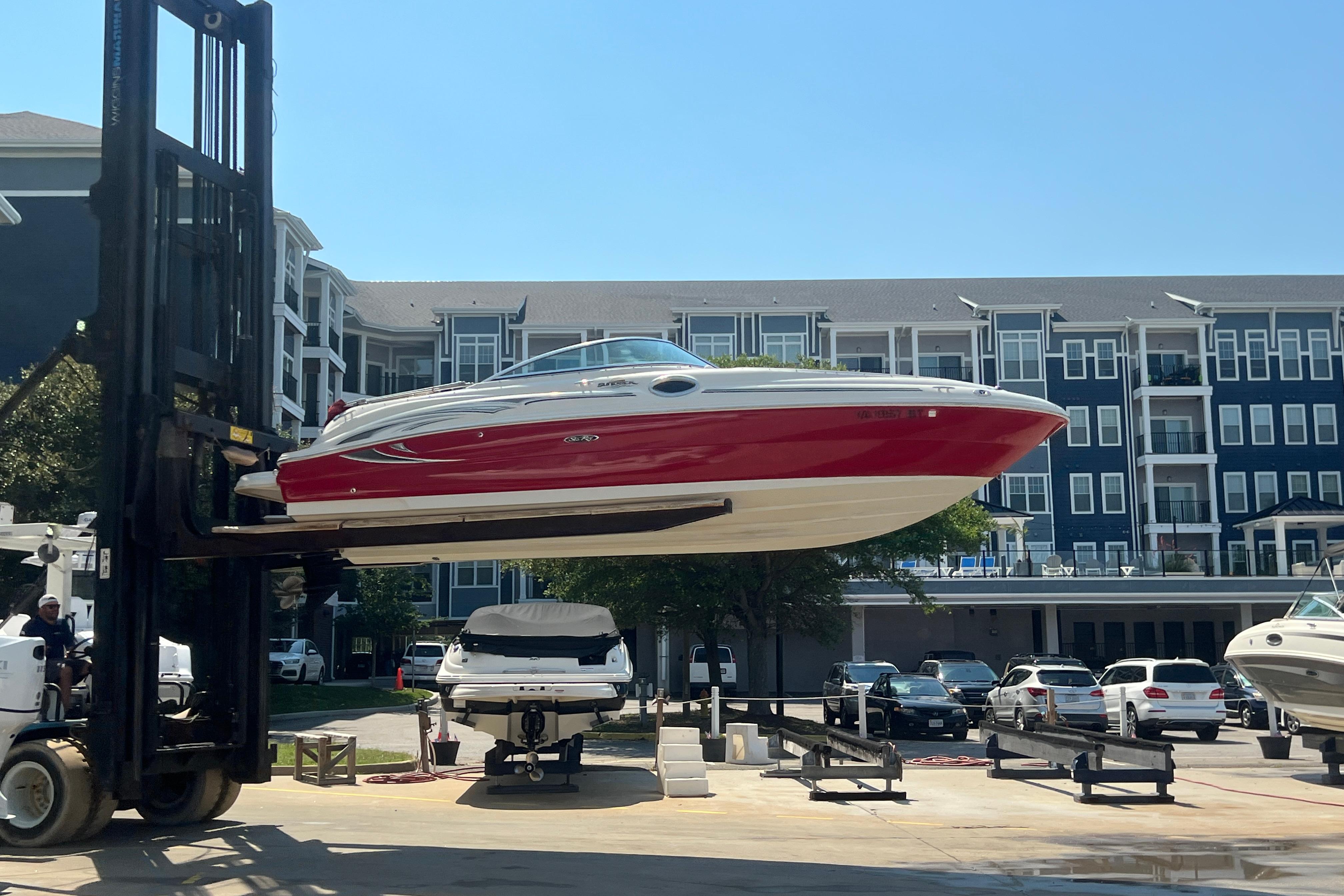 2005 Sea Ray 240 Sundeck boat lifted by forklift near waterfront apartments.