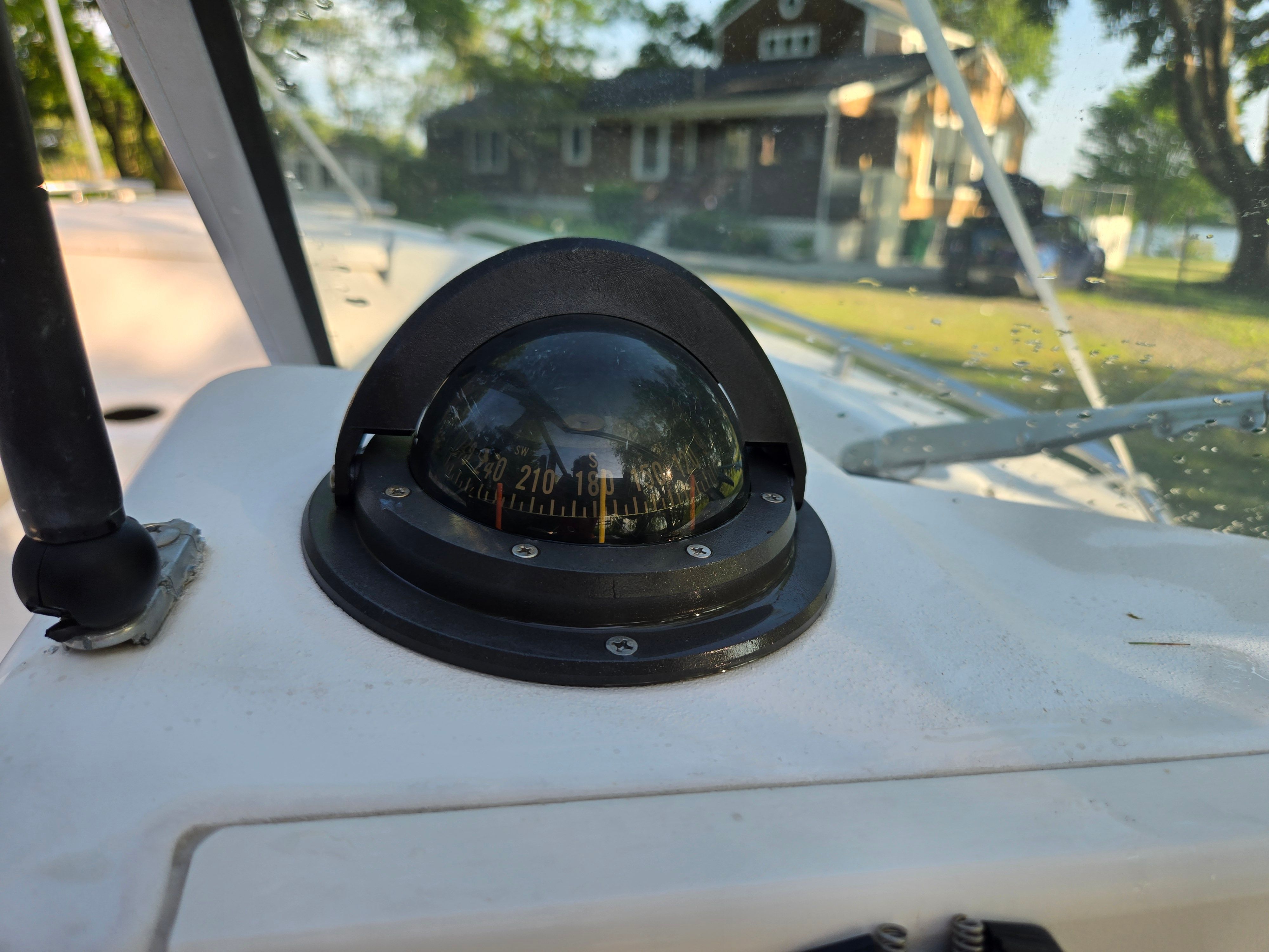 A compass on a boat with houses in the background.