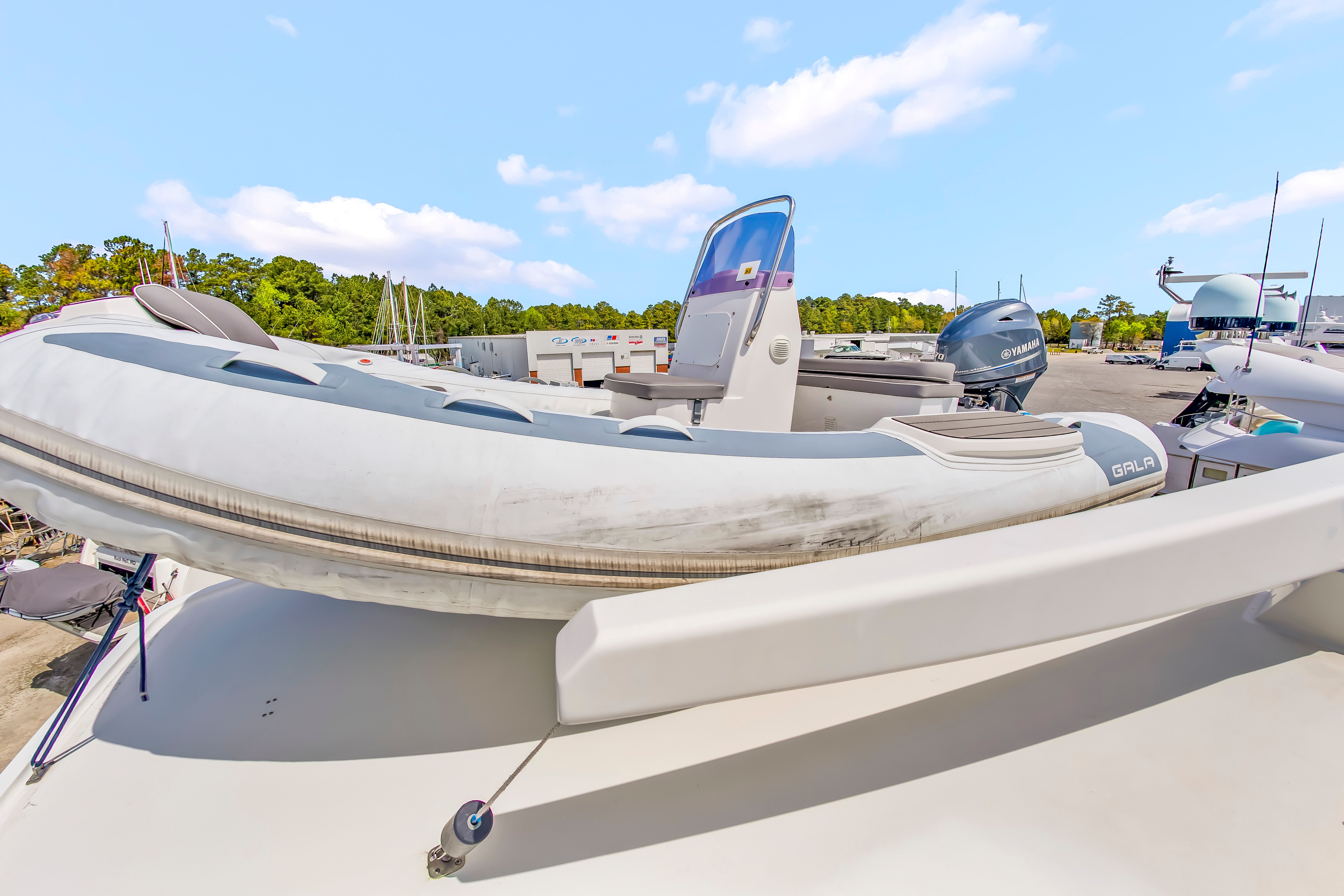 An inflatable boat is secured on a yacht's deck, surrounded by trees and a clear sky.