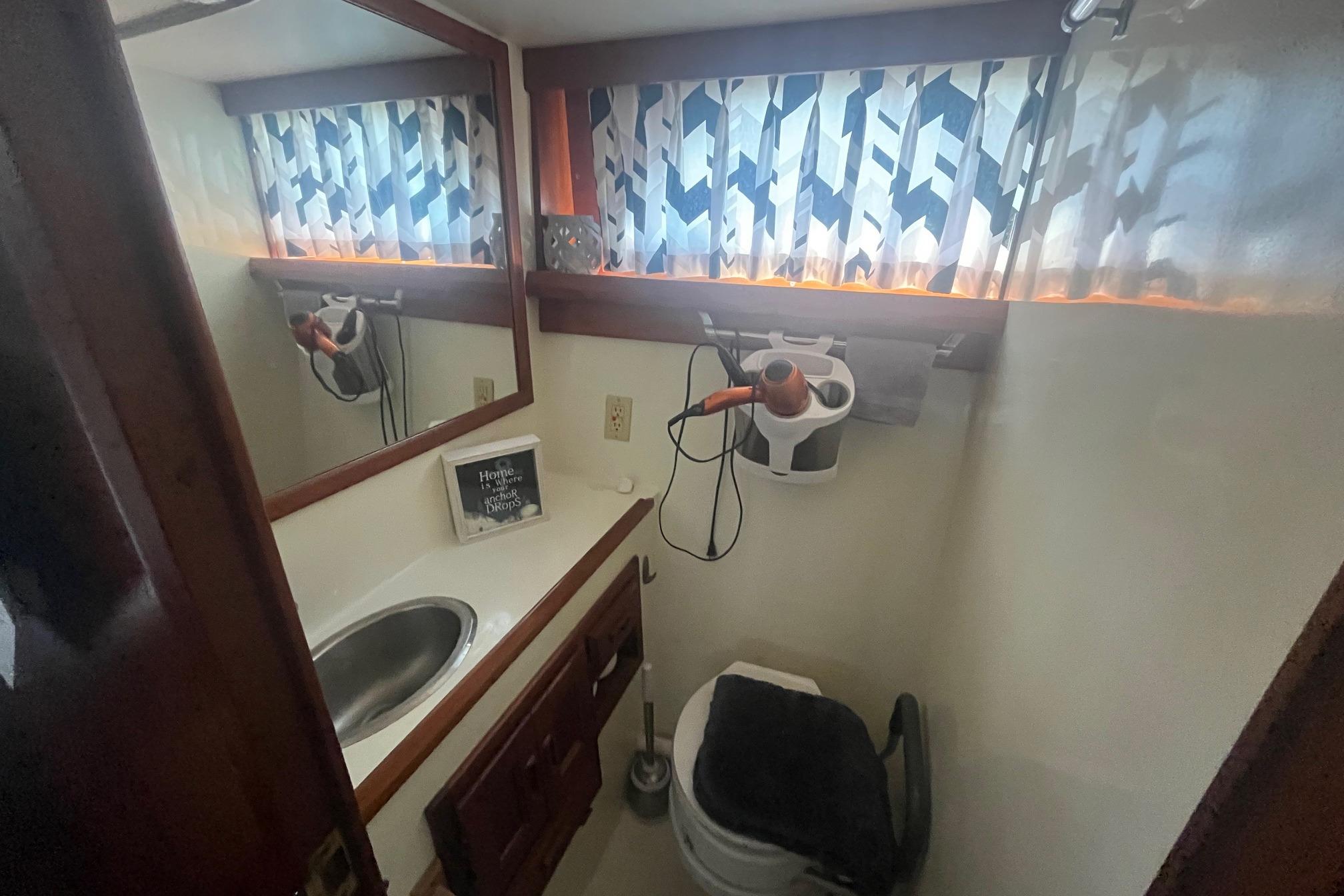 Compact bathroom in 1990 Cooper Prowler 35 boat with sink, toilet, and patterned curtains.