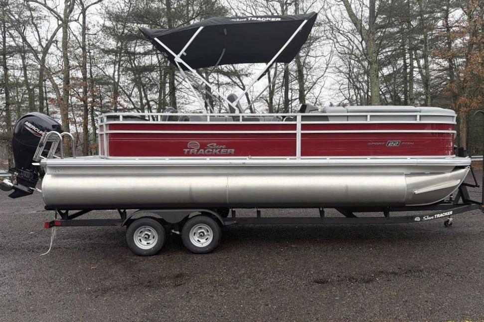 2026 Sun Tracker SportFish 22 DLX pontoon boat on trailer, parked outdoors.