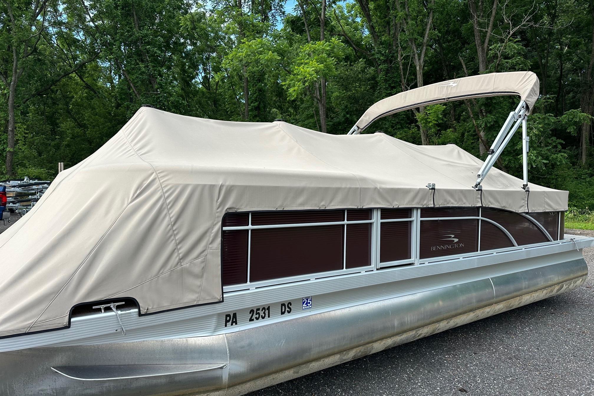 2016 Bennington 24 SCWX pontoon boat with beige cover, parked on a forested road.