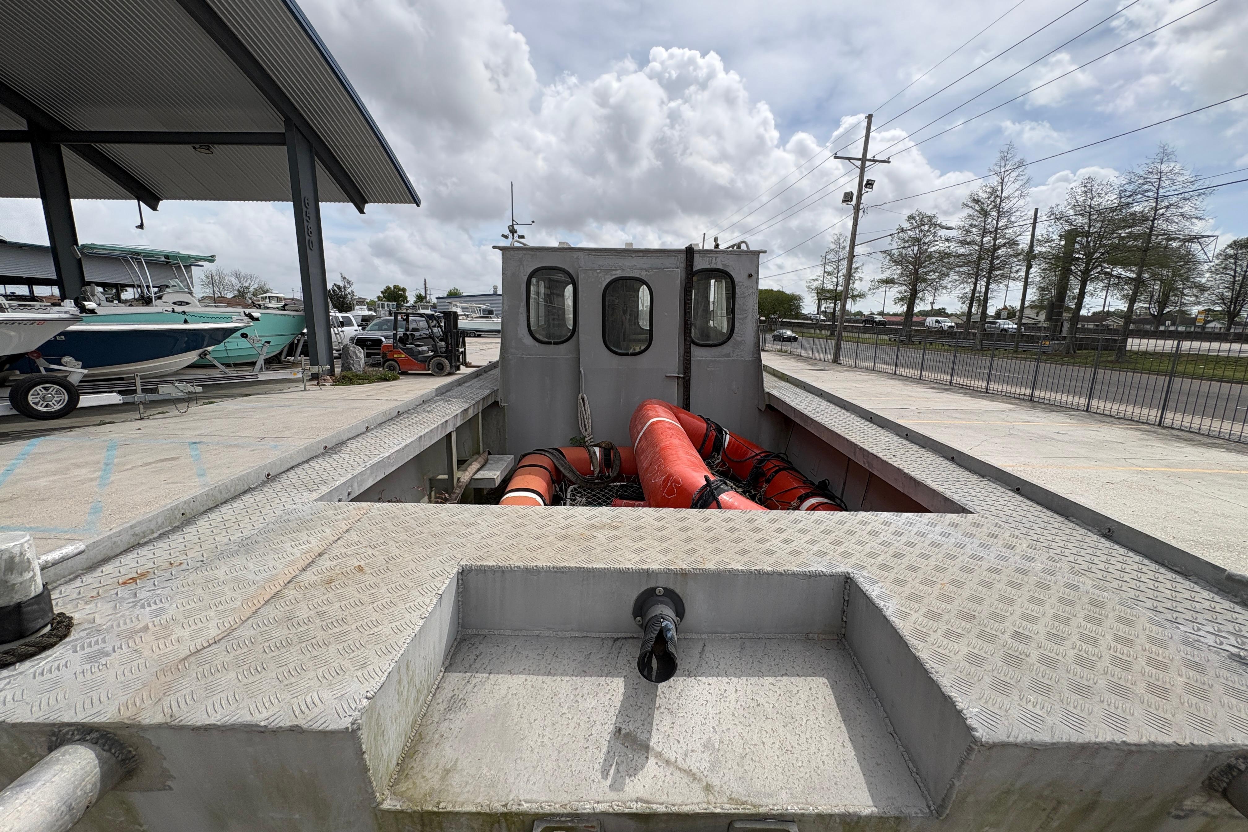 1972 Custom 23' work/push boat with metal deck, docked outdoors under cloudy sky.