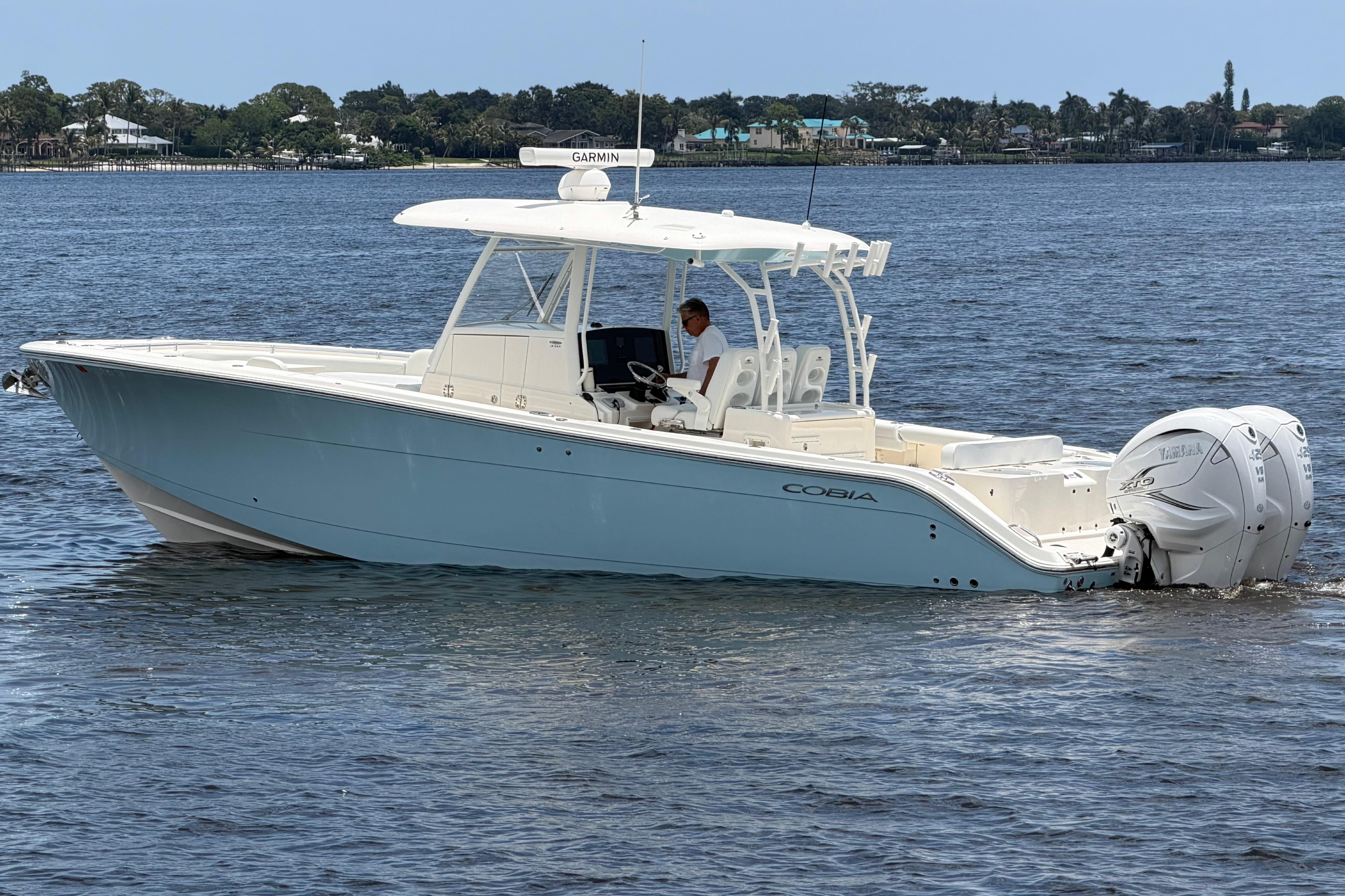 2023 Cobia 350 Center Console boat cruising on a calm lake with scenic background.