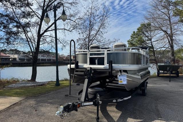 2026 Sun Tracker Bass Buggy 16 XL Select pontoon boat on trailer by a lakeside.