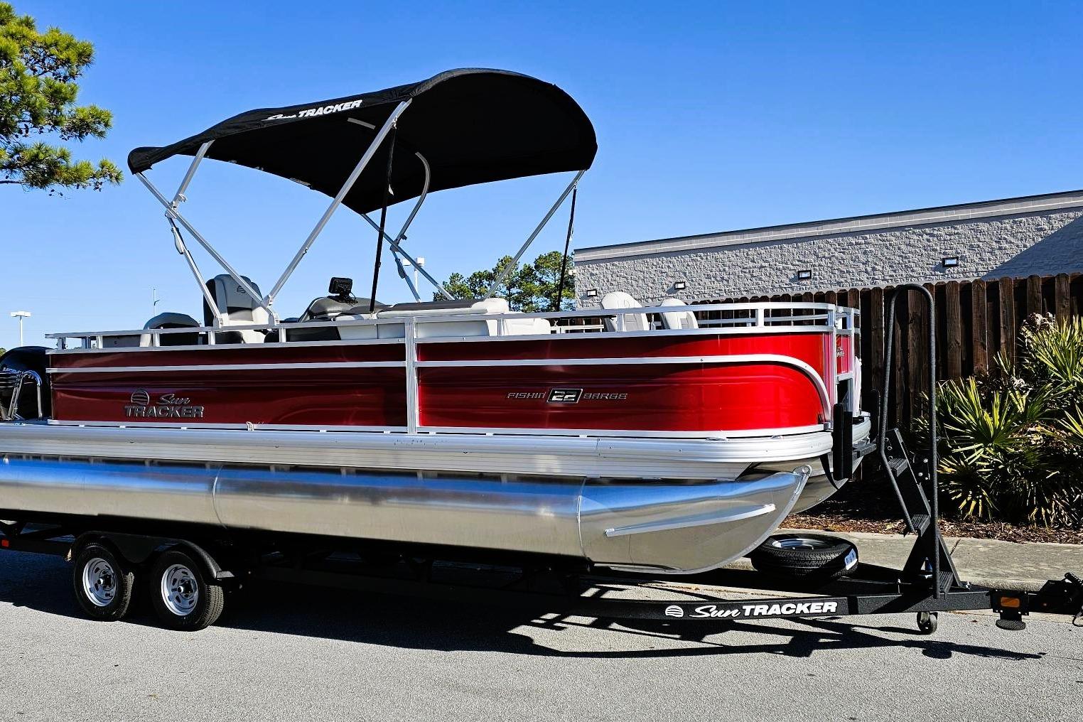 2026 Sun Tracker Fishin' Barge 22 DLX pontoon boat on trailer, red and silver design.