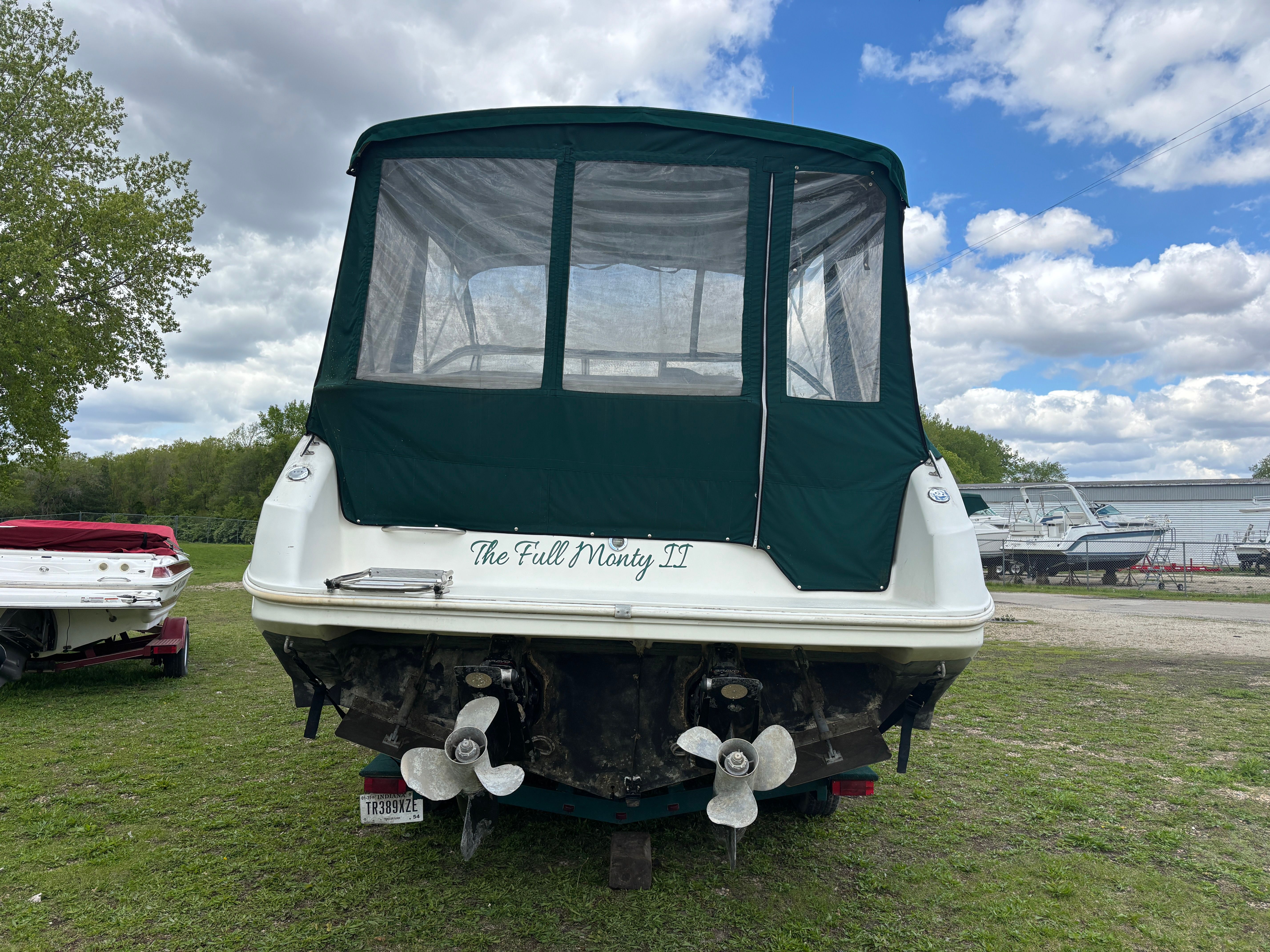 A boat with a green canopy is on grass, surrounded by trees and other boats.